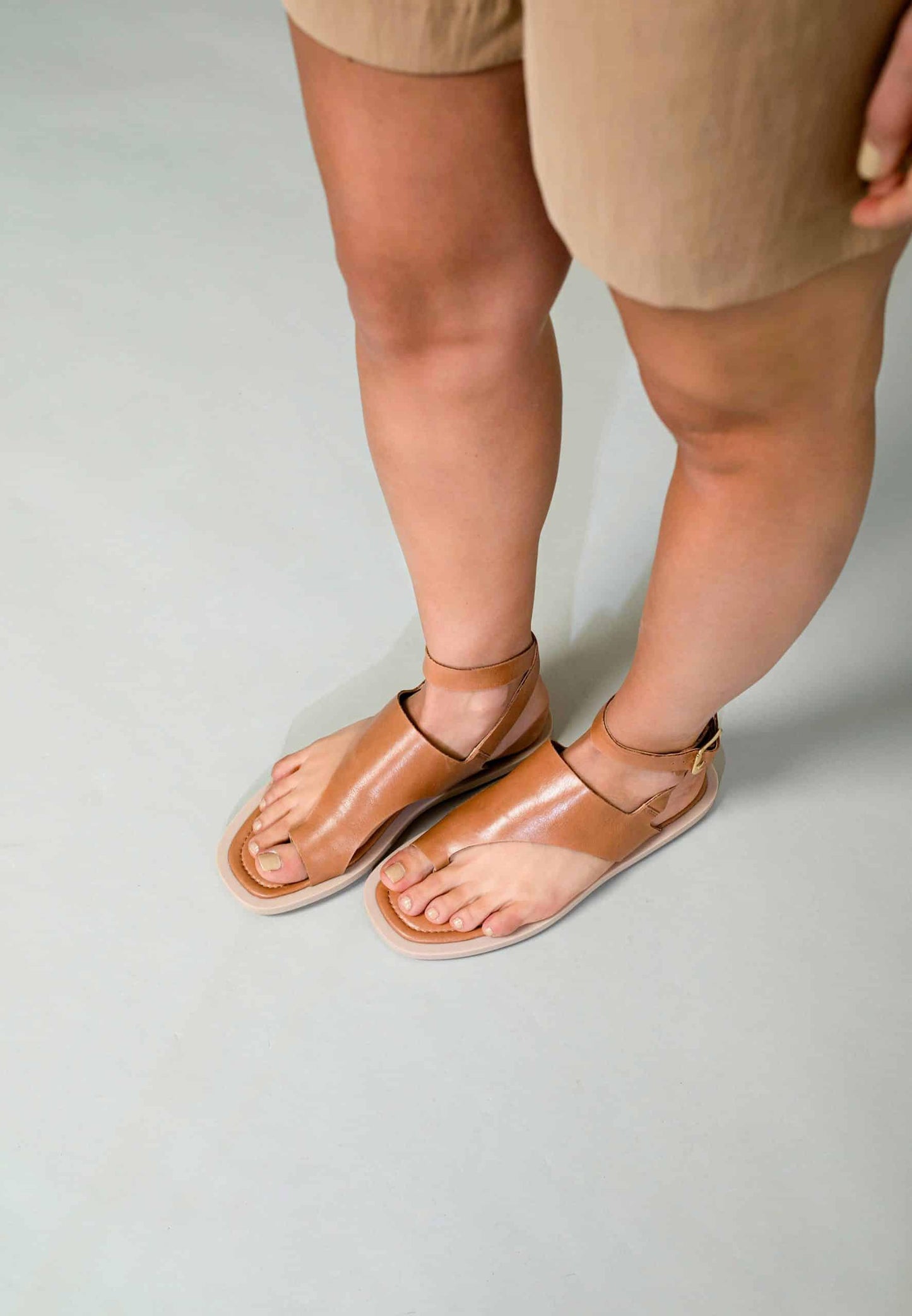 Person wearing tan sandals on a light gray background