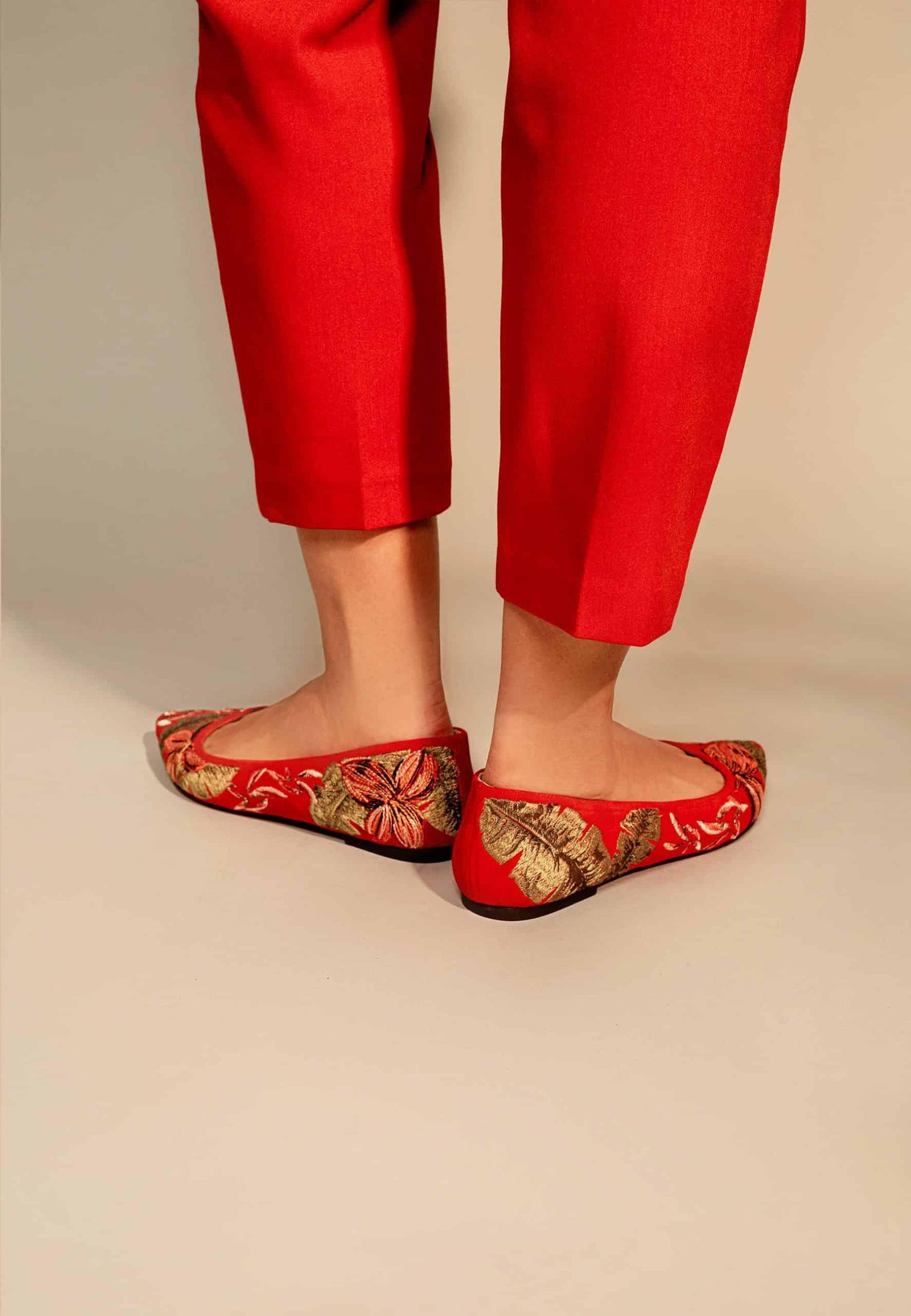 Red embroidered shoes worn with red pants on a beige background