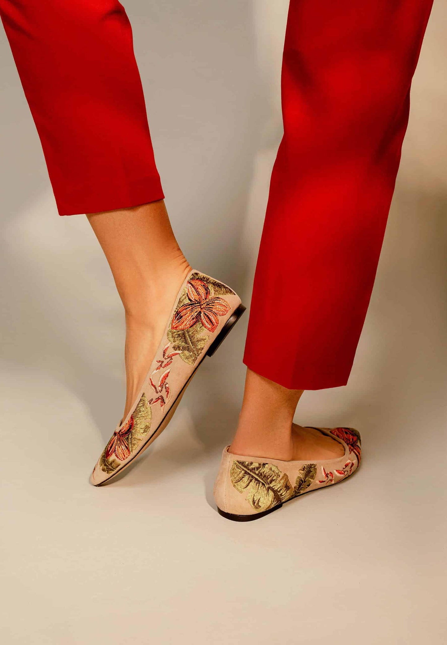Floral-patterned flats worn with red pants on a neutral background