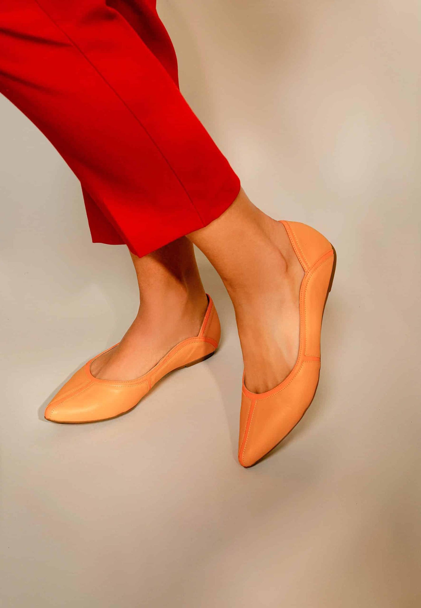 Orange flats worn with red pants on a neutral background