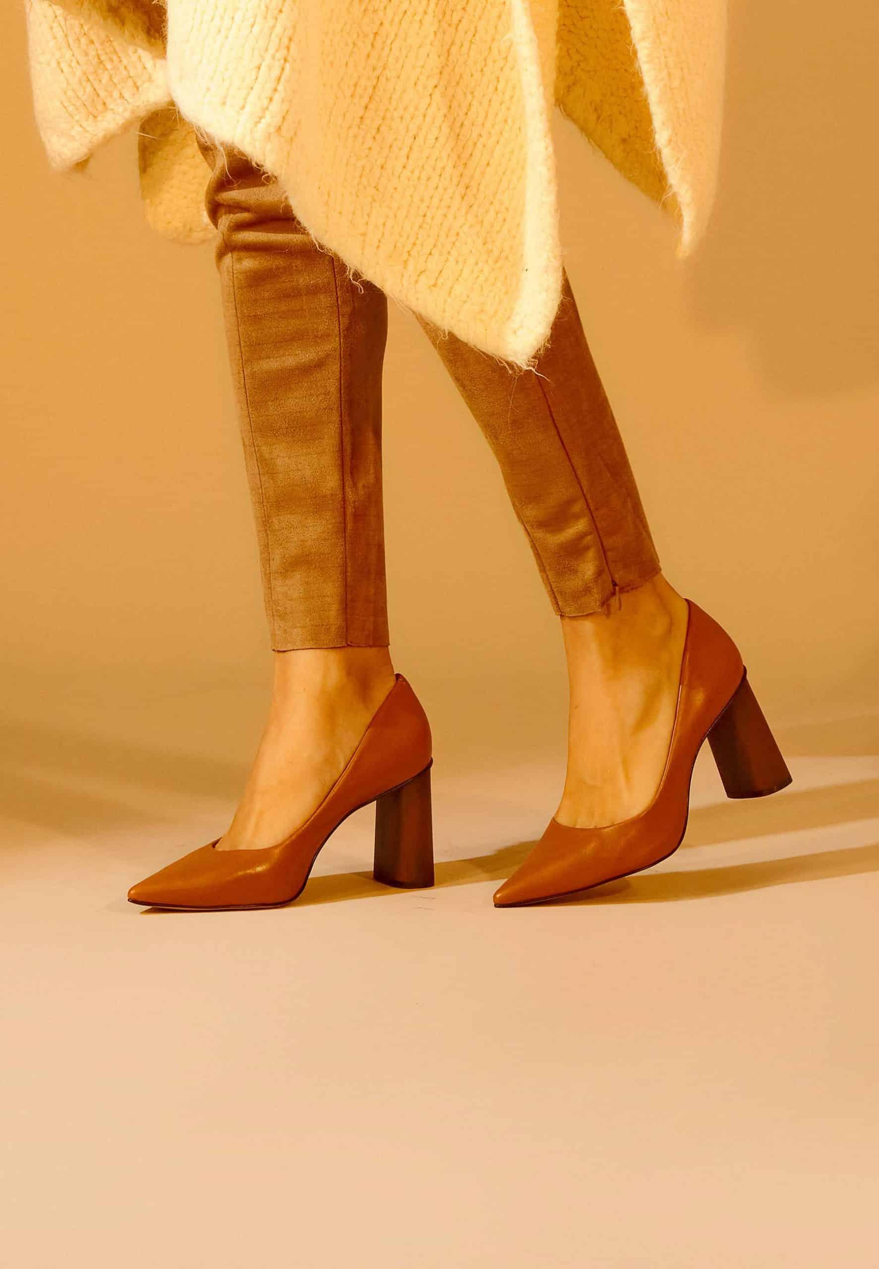 Brown high-heeled shoes worn with beige pants and a light coat on a beige background