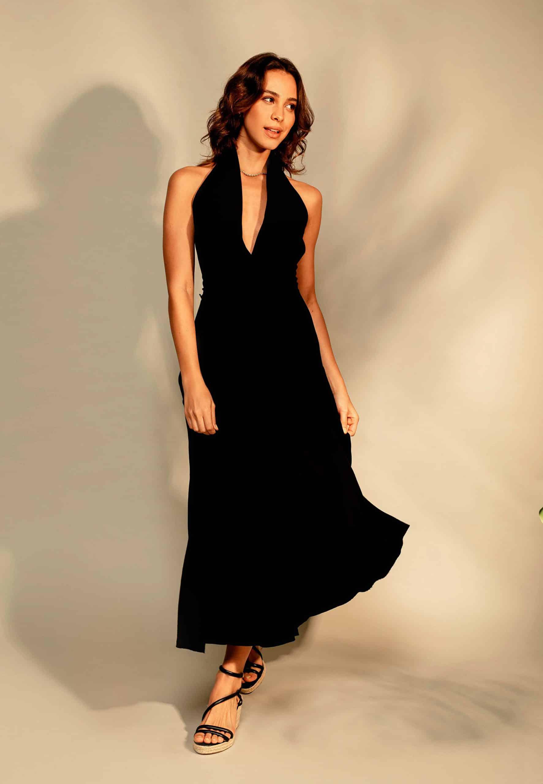 Woman wearing a black halter neck dress against a neutral background