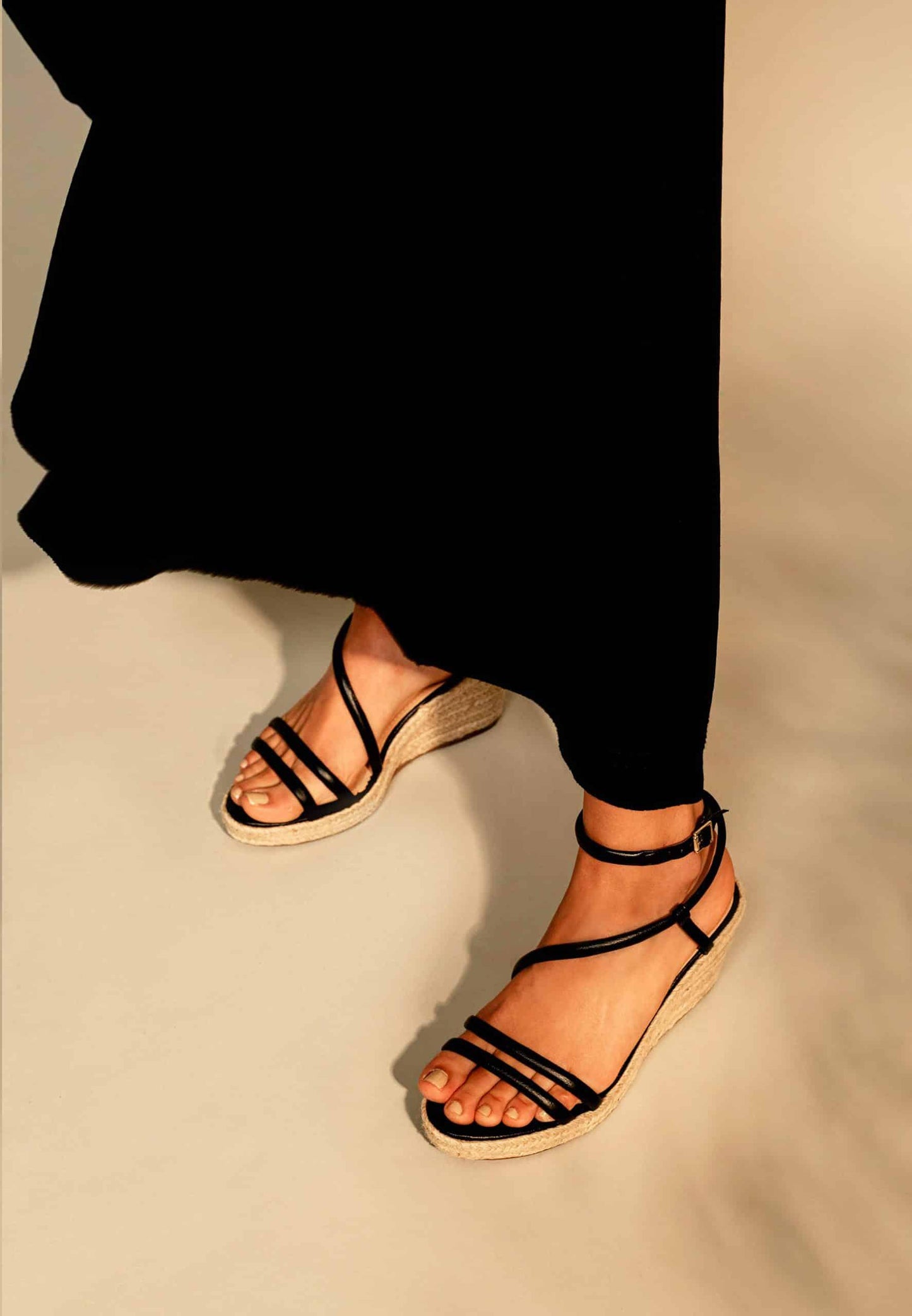 Black strappy sandals worn with black pants on a neutral background