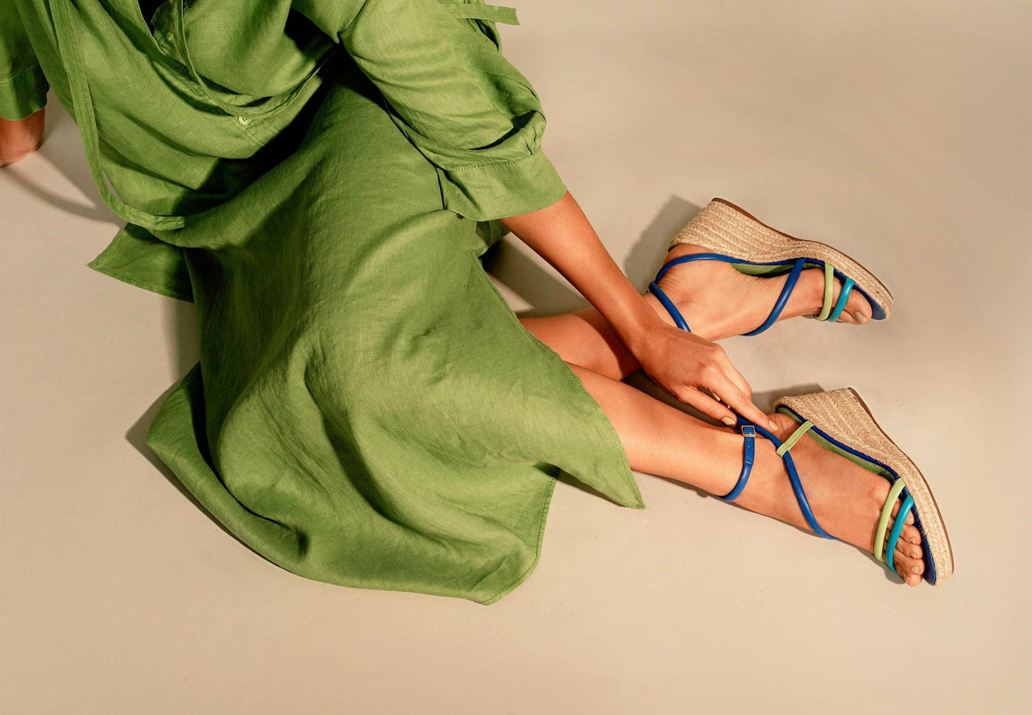 Person wearing green shoes with blue straps sitting on a light-colored floor.