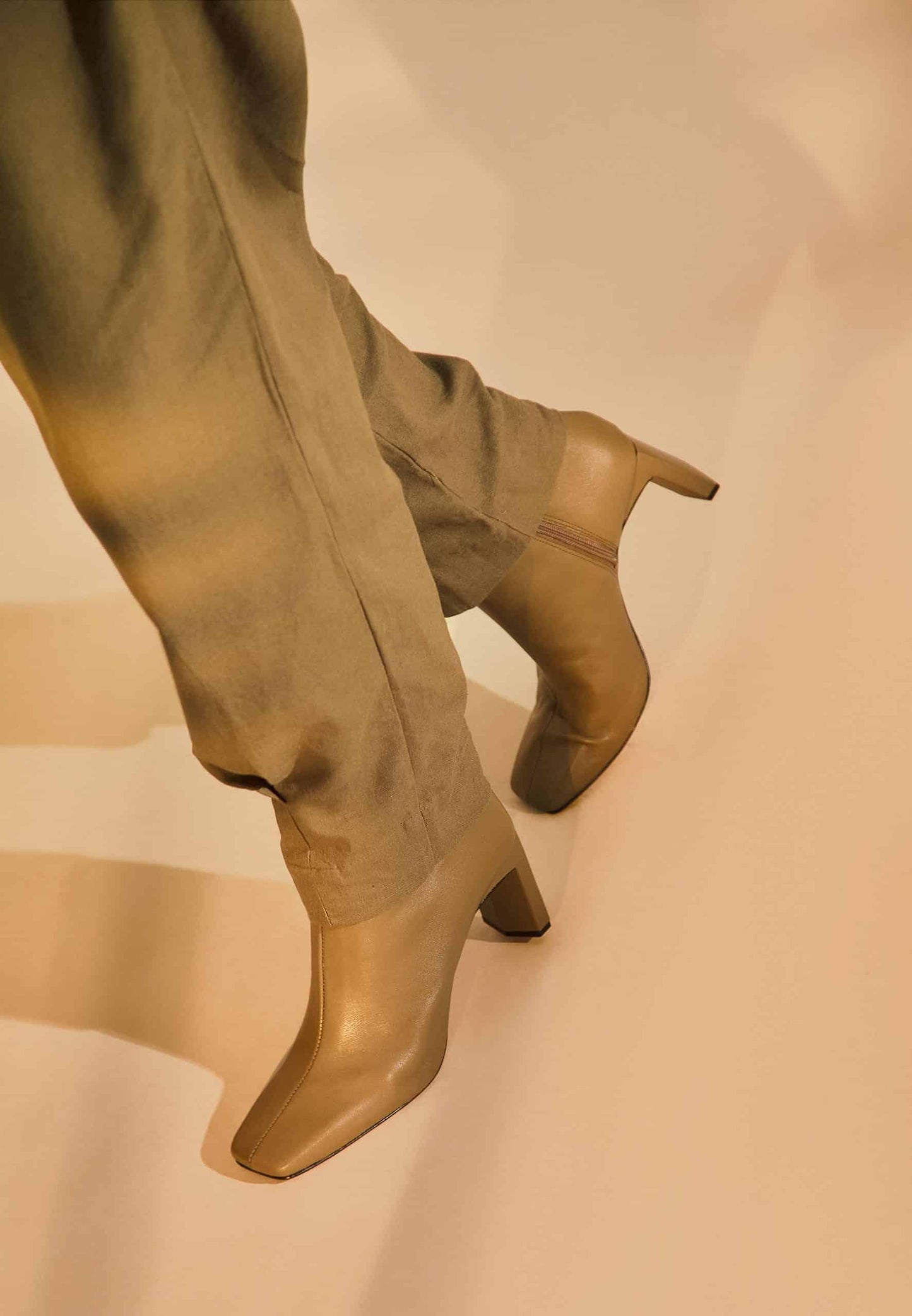 Gold high-heeled boots worn with matching pants on a beige background