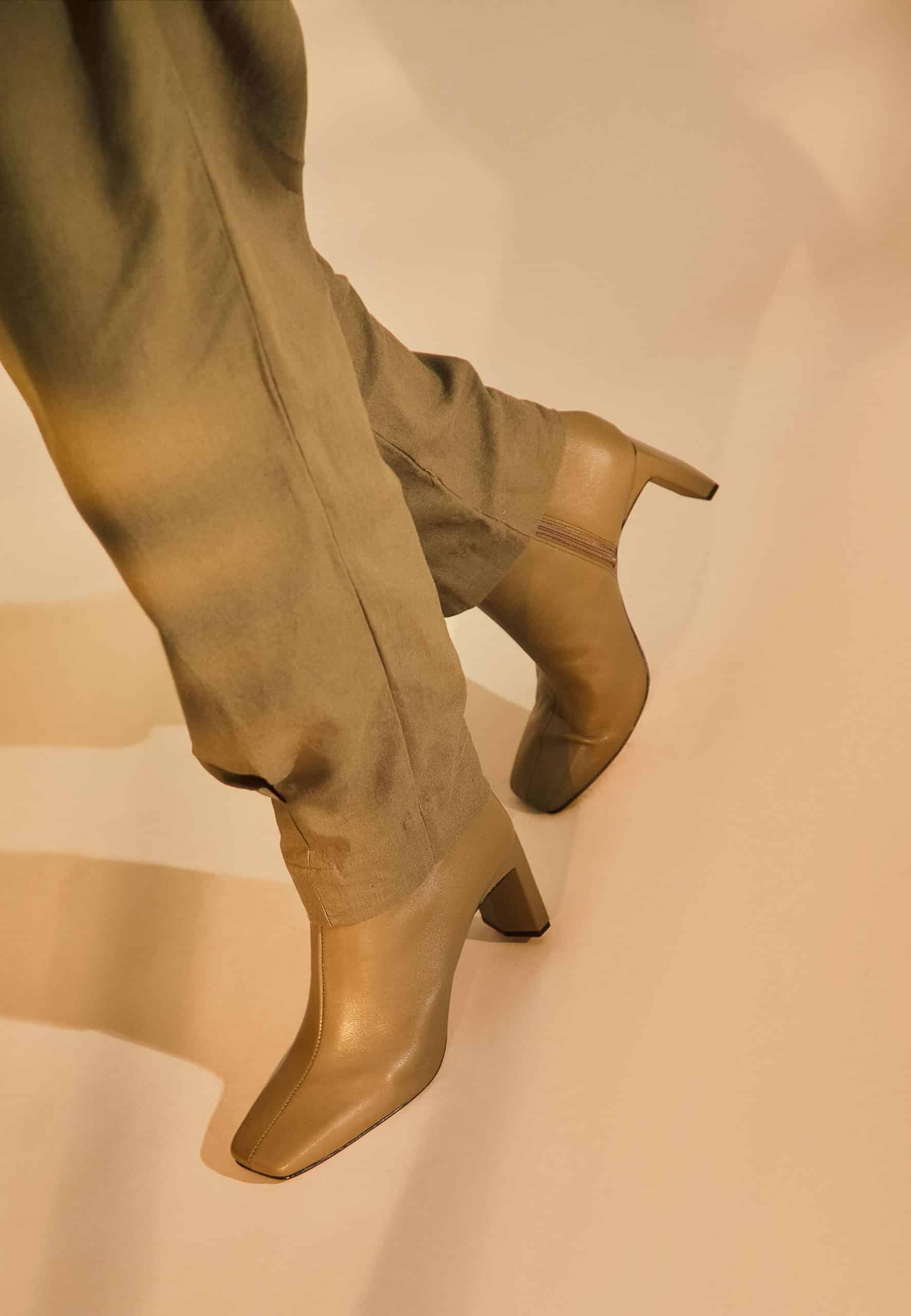 Gold high-heeled boots worn with matching pants on a beige background