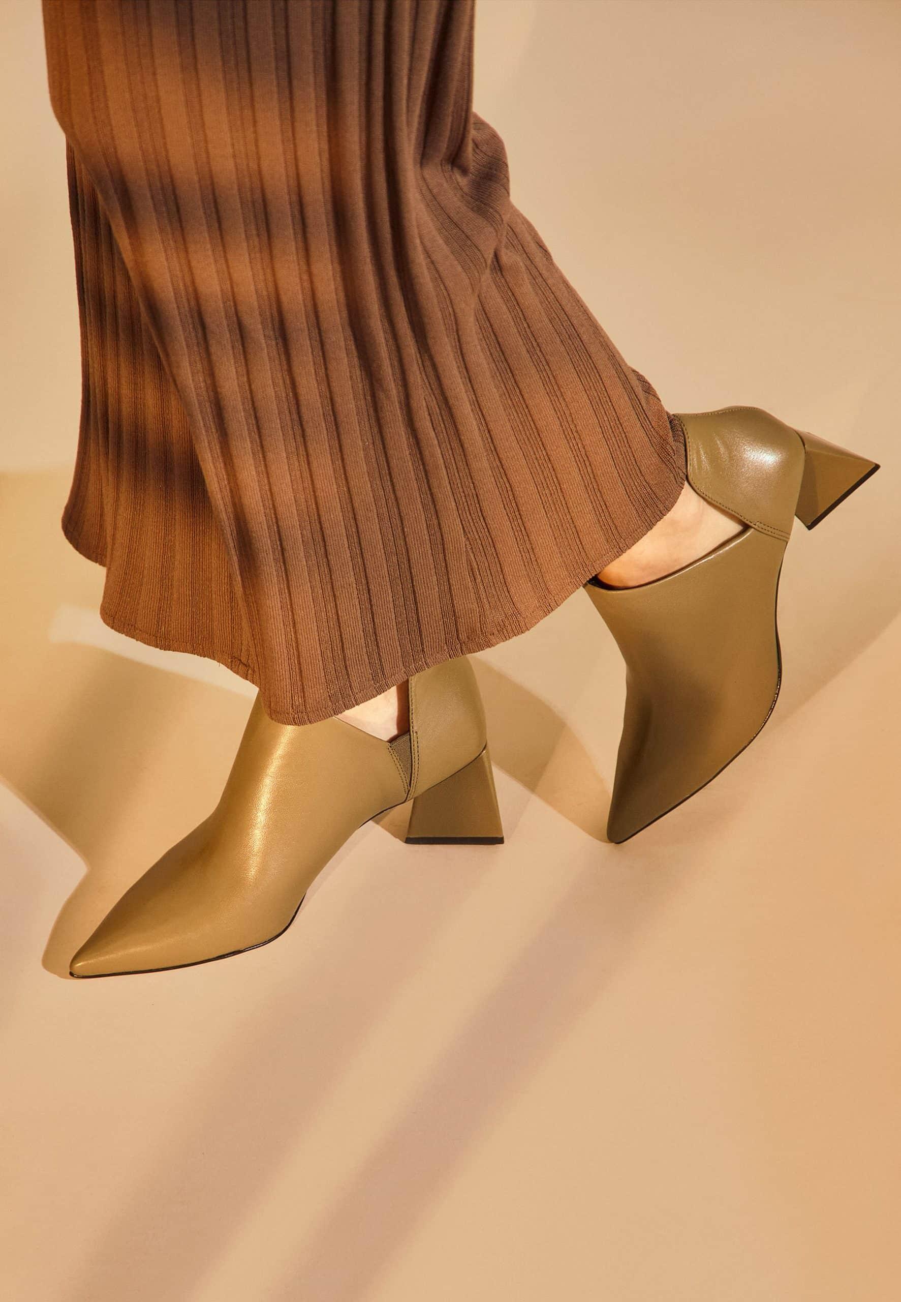 Gold high-heeled shoes worn with a pleated brown skirt on a beige background