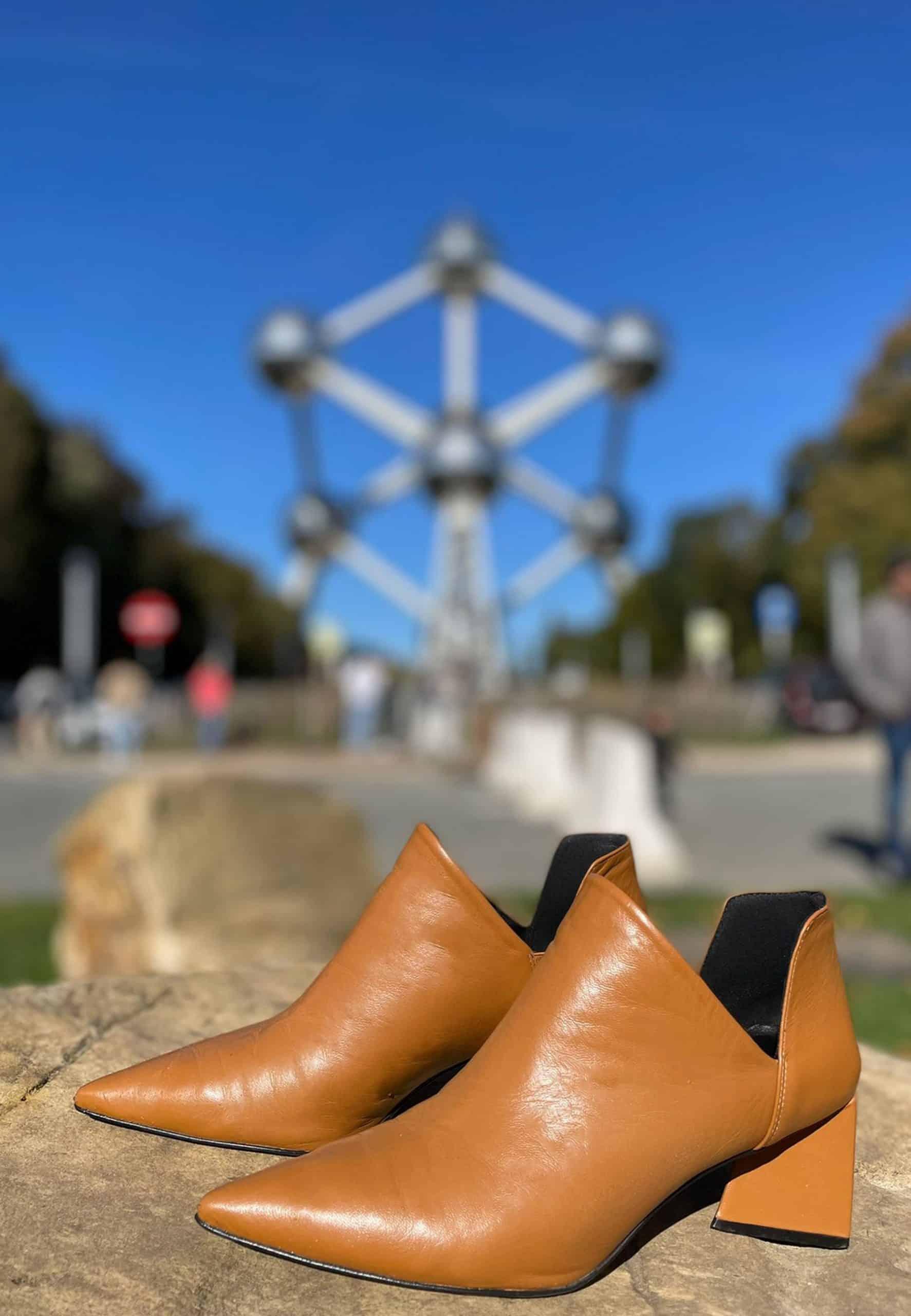 Pair of brown leather shoes on a stone surface with a blurred background featuring a modern sculpture.