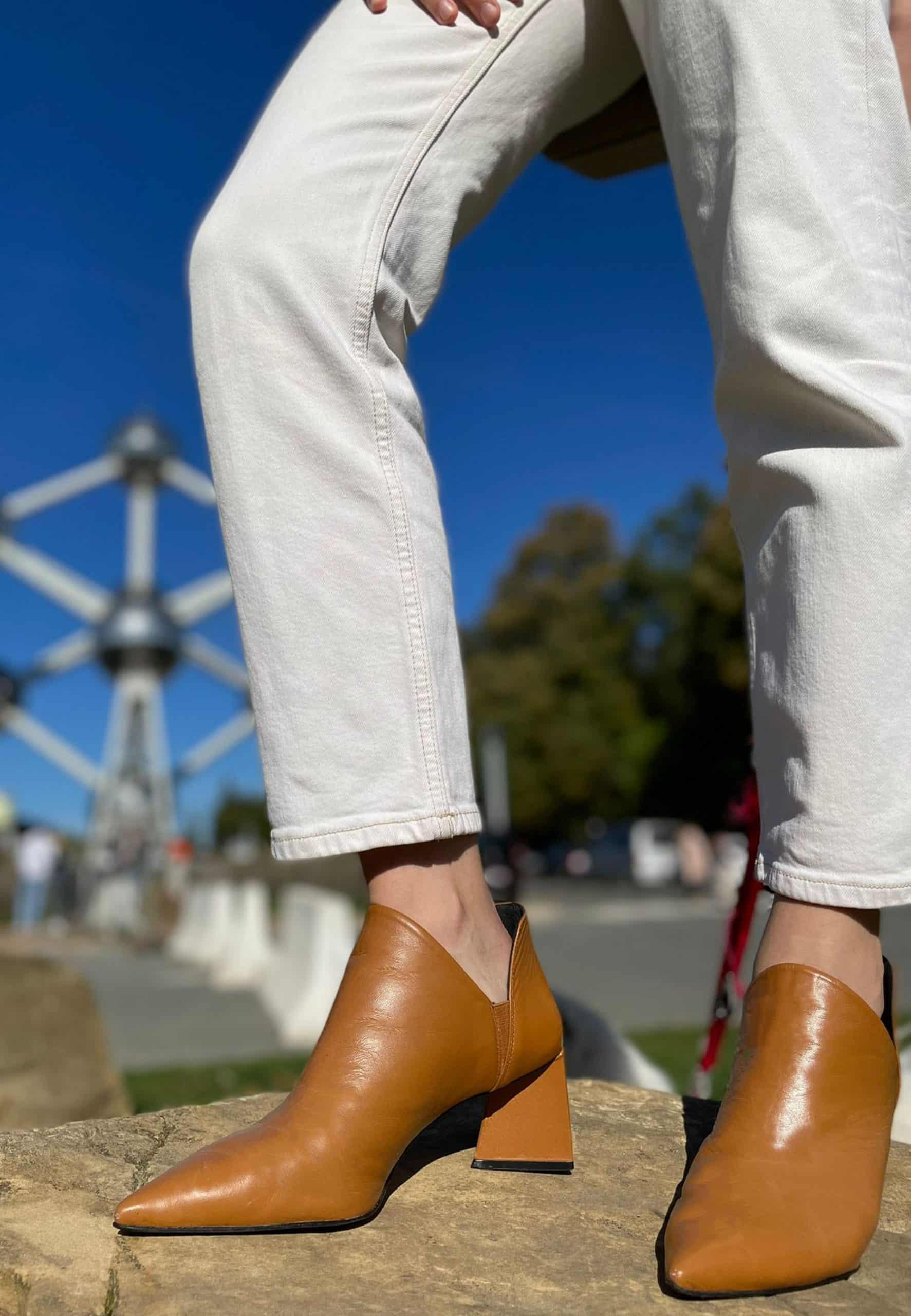 Brown leather ankle boots worn with light-colored pants against a blurred outdoor background