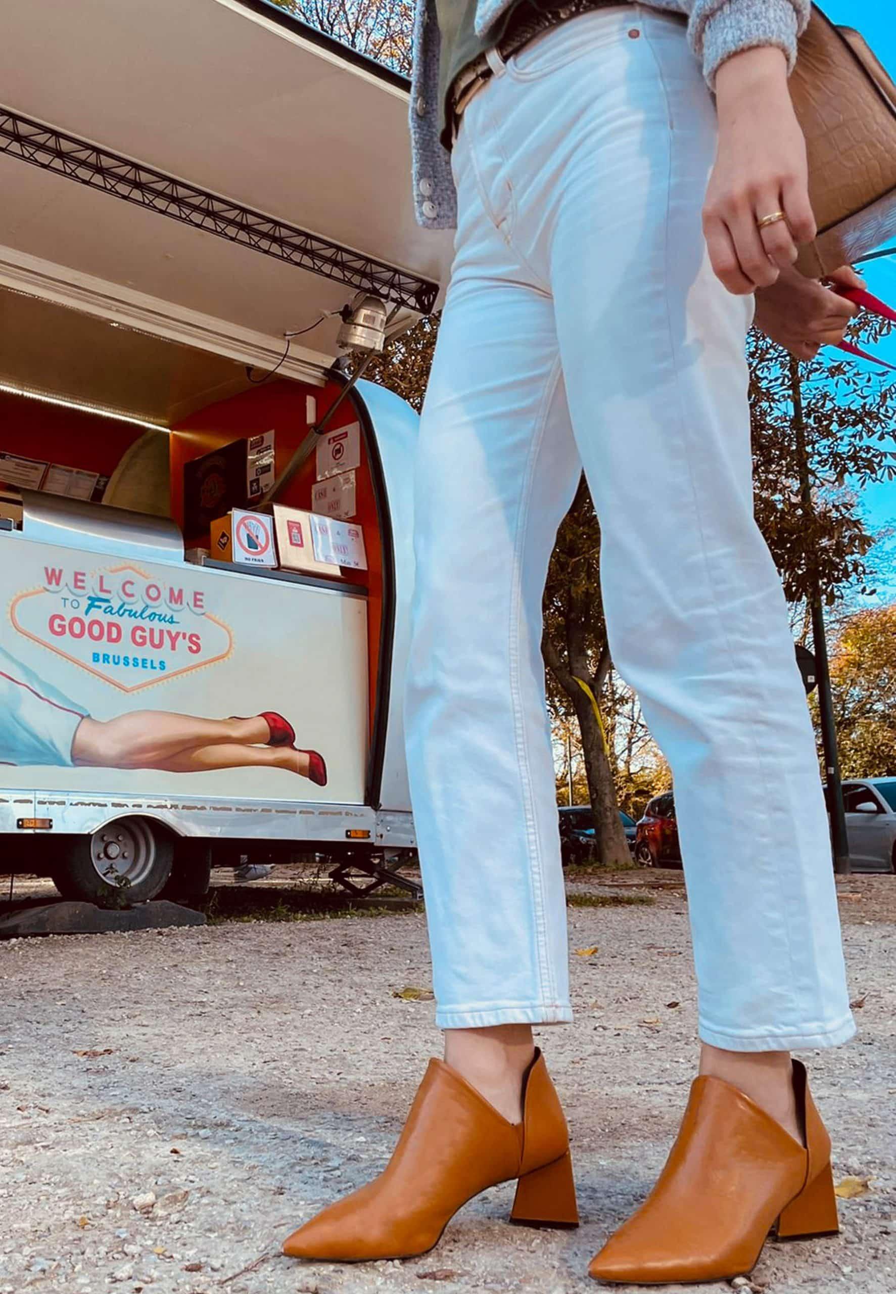 Person wearing light blue jeans and brown boots standing in front of a food truck with an advertisement.