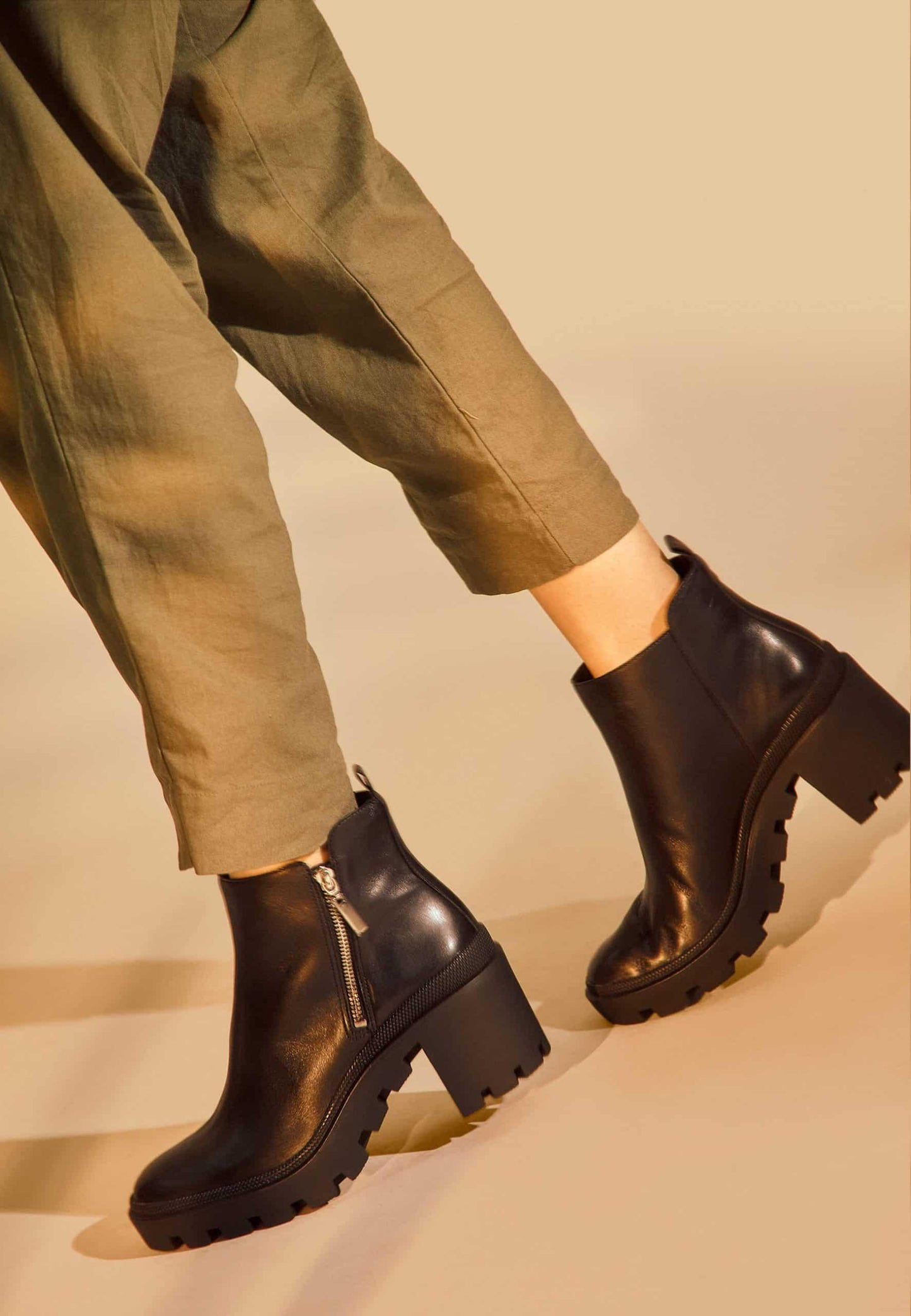 Black chunky boots worn with green pants on a beige background
