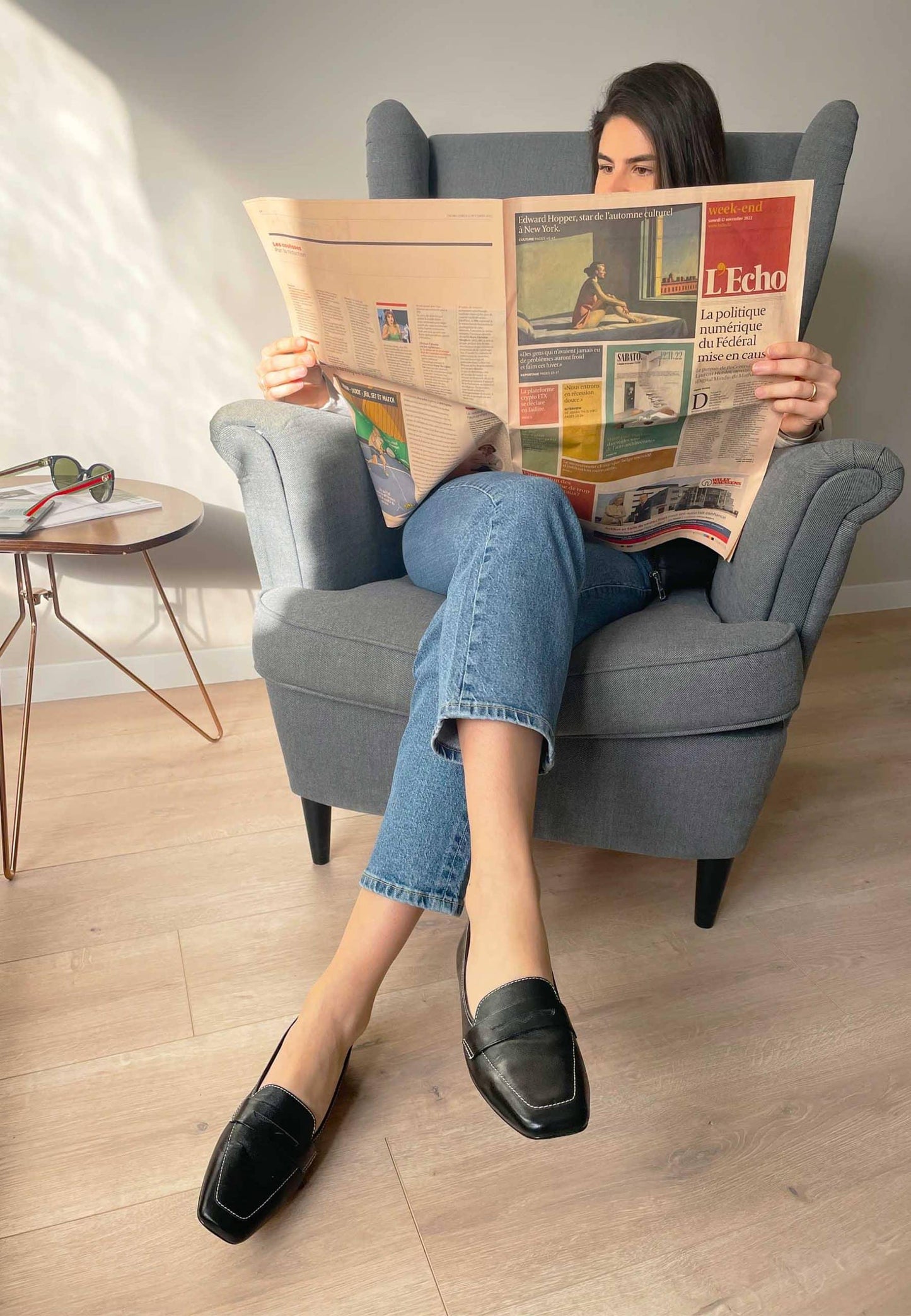 Woman reading a newspaper in a gray armchair