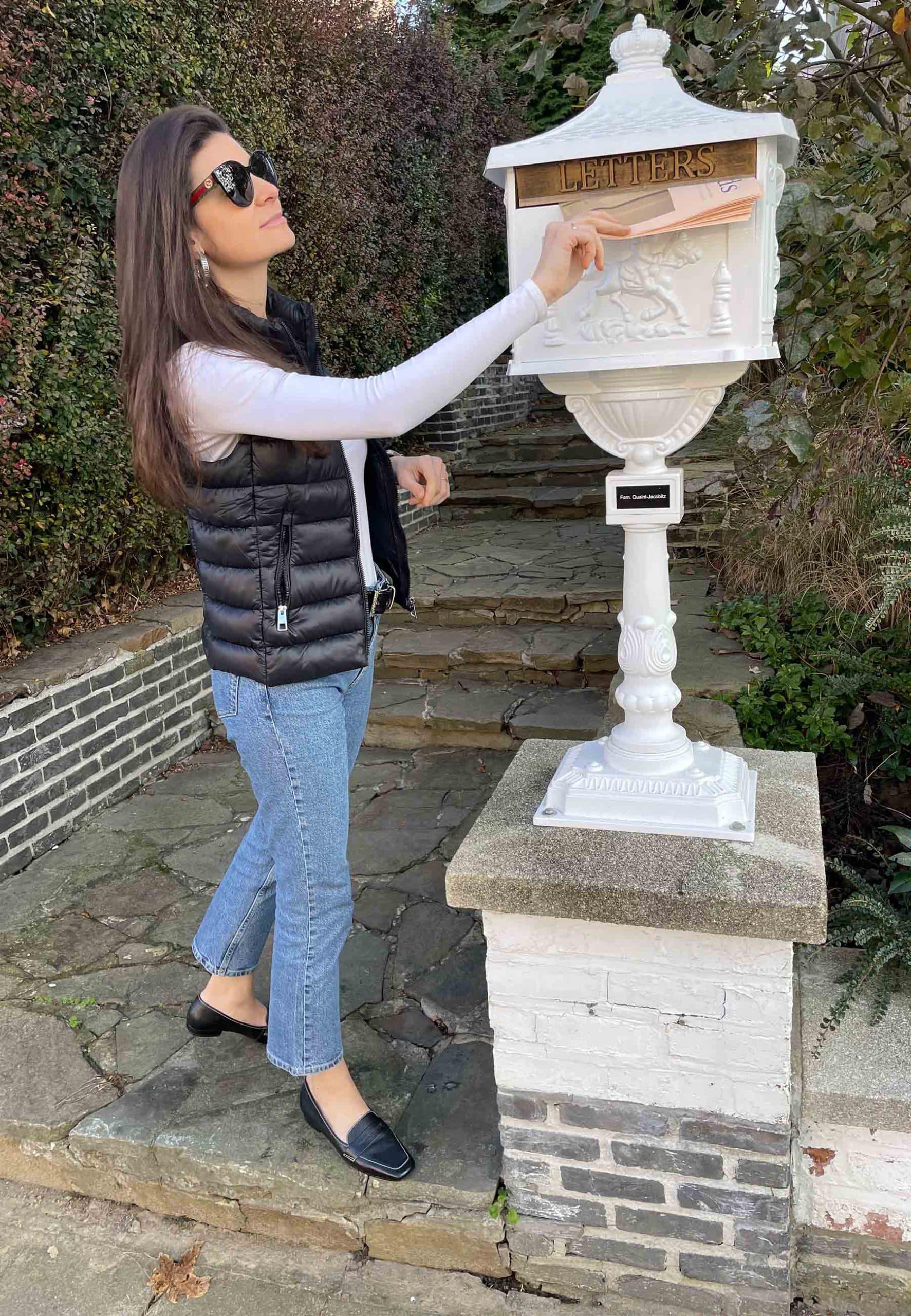 Woman interacting with a decorative mailbox outdoors.