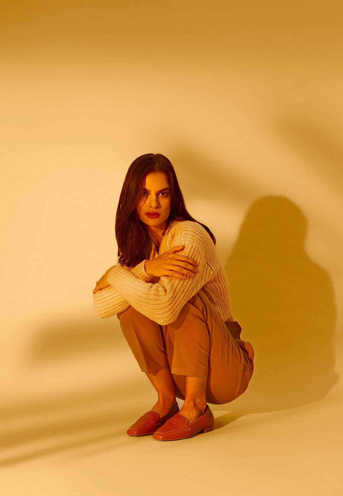 Woman squatting on a yellow background with a warm, soft light