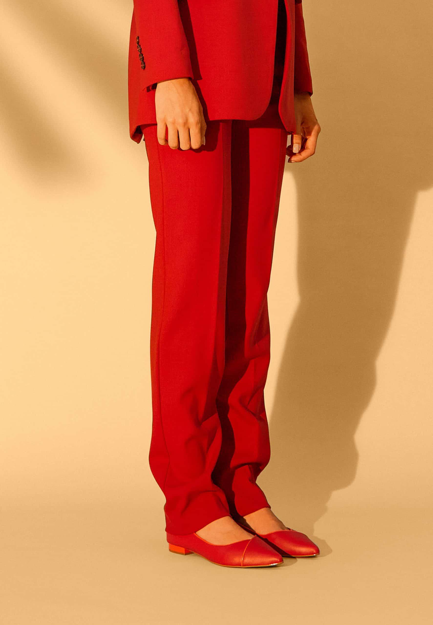 Person wearing a red suit with matching shoes on a beige background