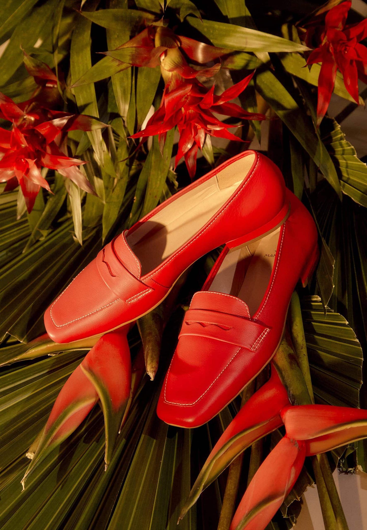 Red loafers on a bed of tropical flowers and leaves