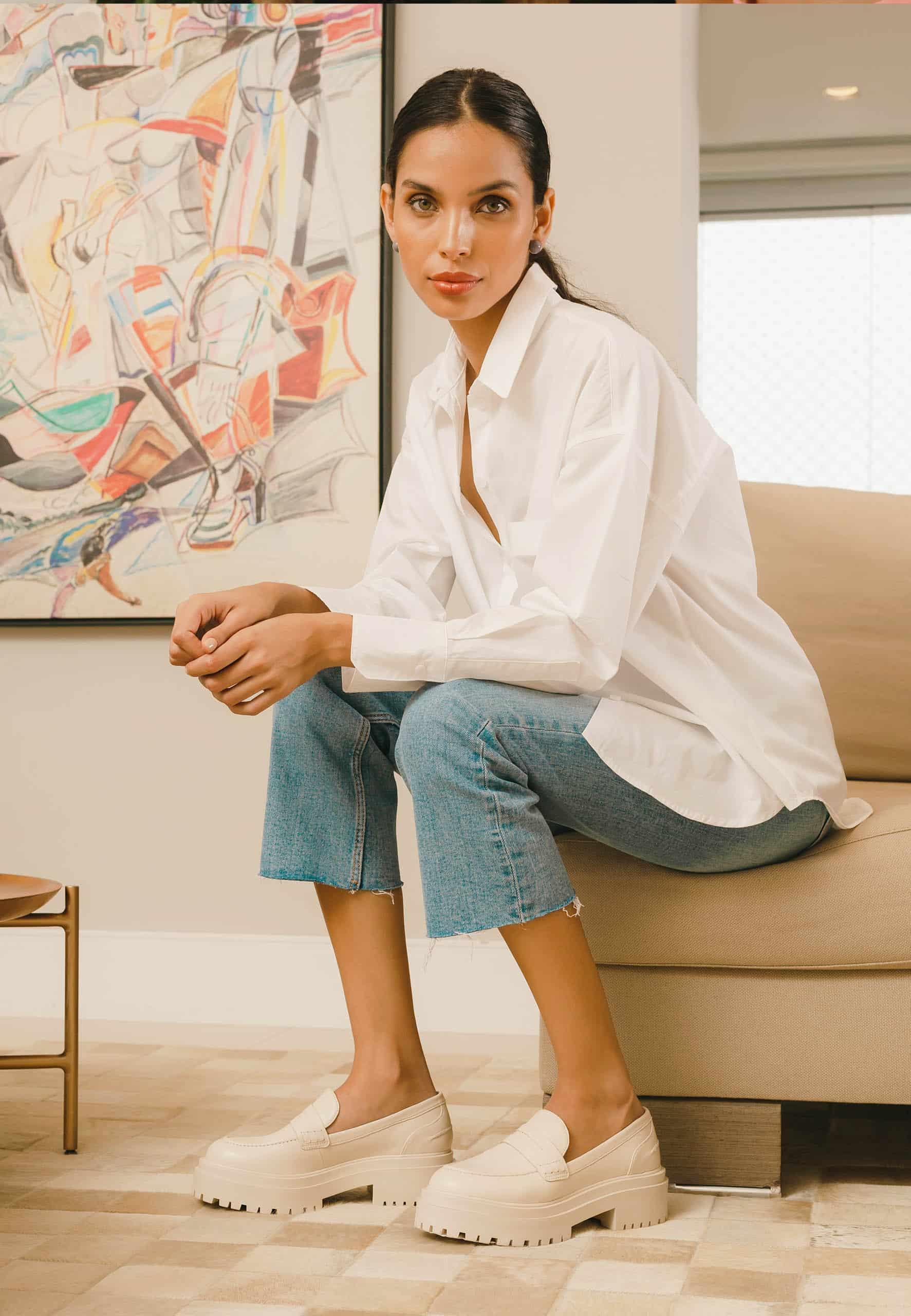 Woman sitting on a couch wearing a white shirt and blue jeans in a modern living room.