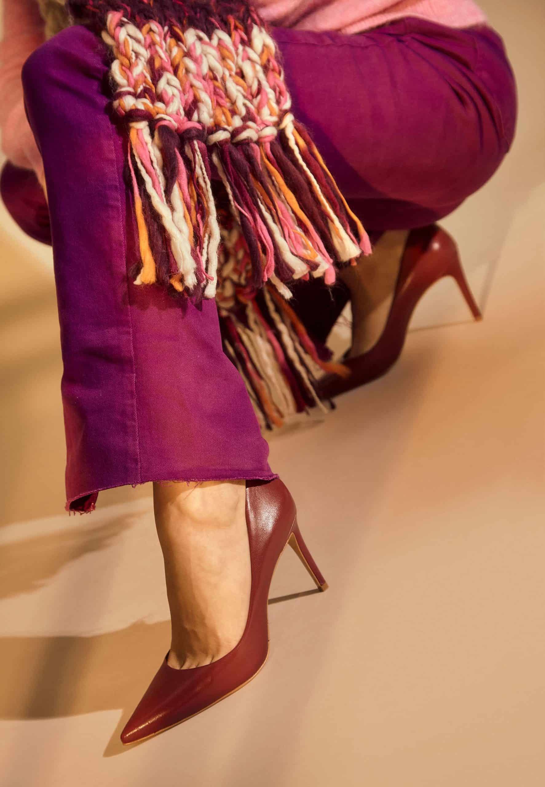 Person wearing a colorful scarf, purple skirt, and red high heels on a neutral background
