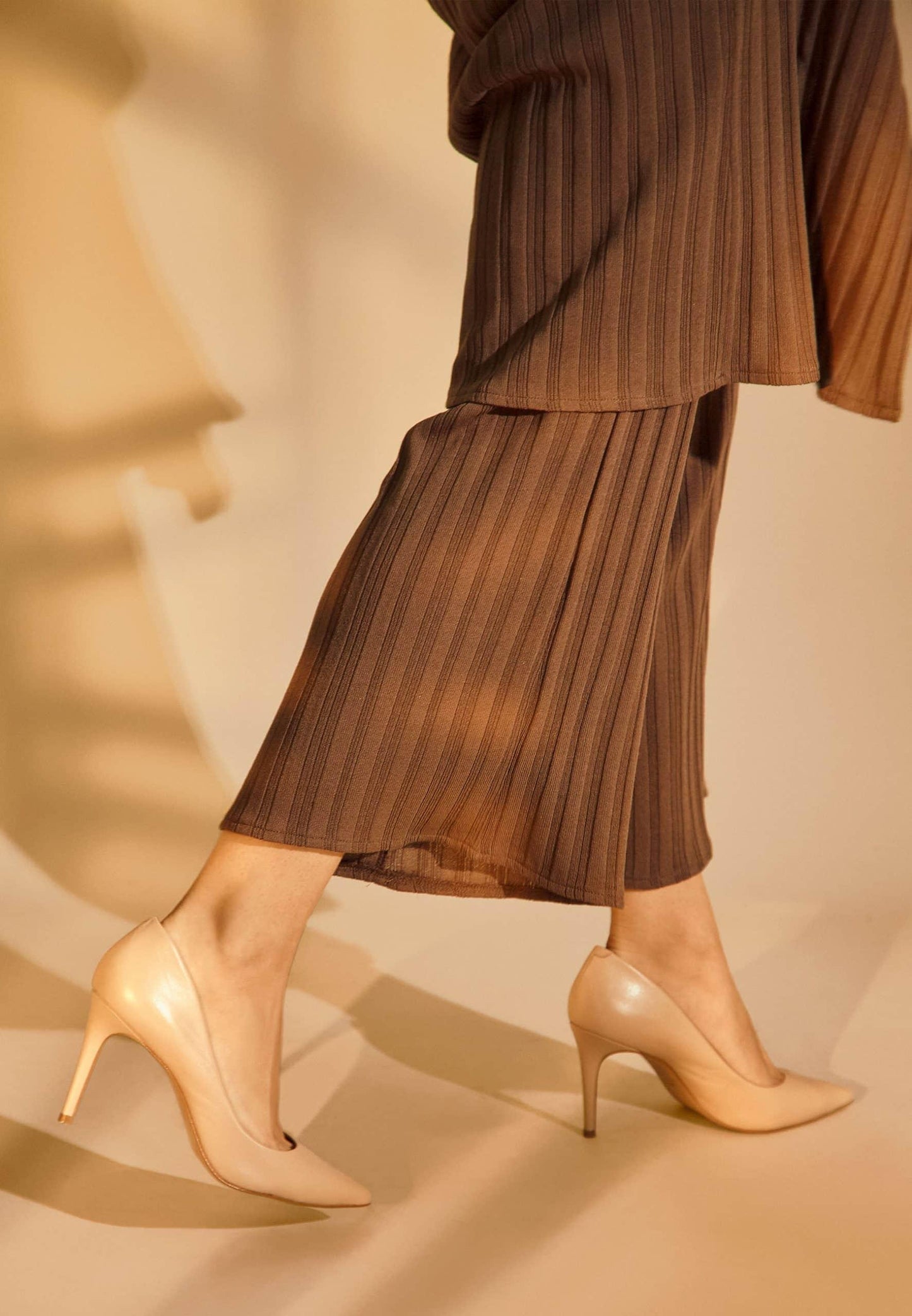 Brown pleated pants and beige high-heeled shoes on a neutral background