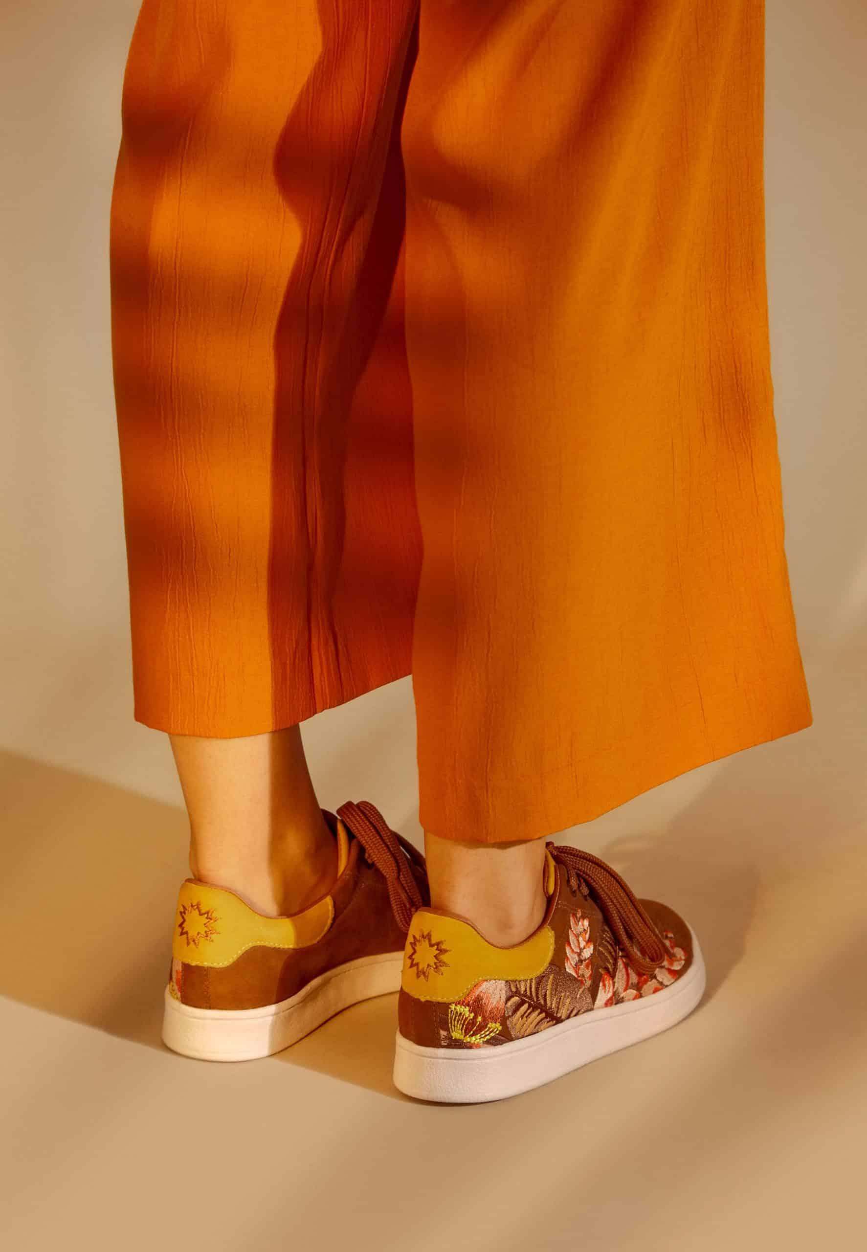 Person wearing floral sneakers with orange pants on a beige background