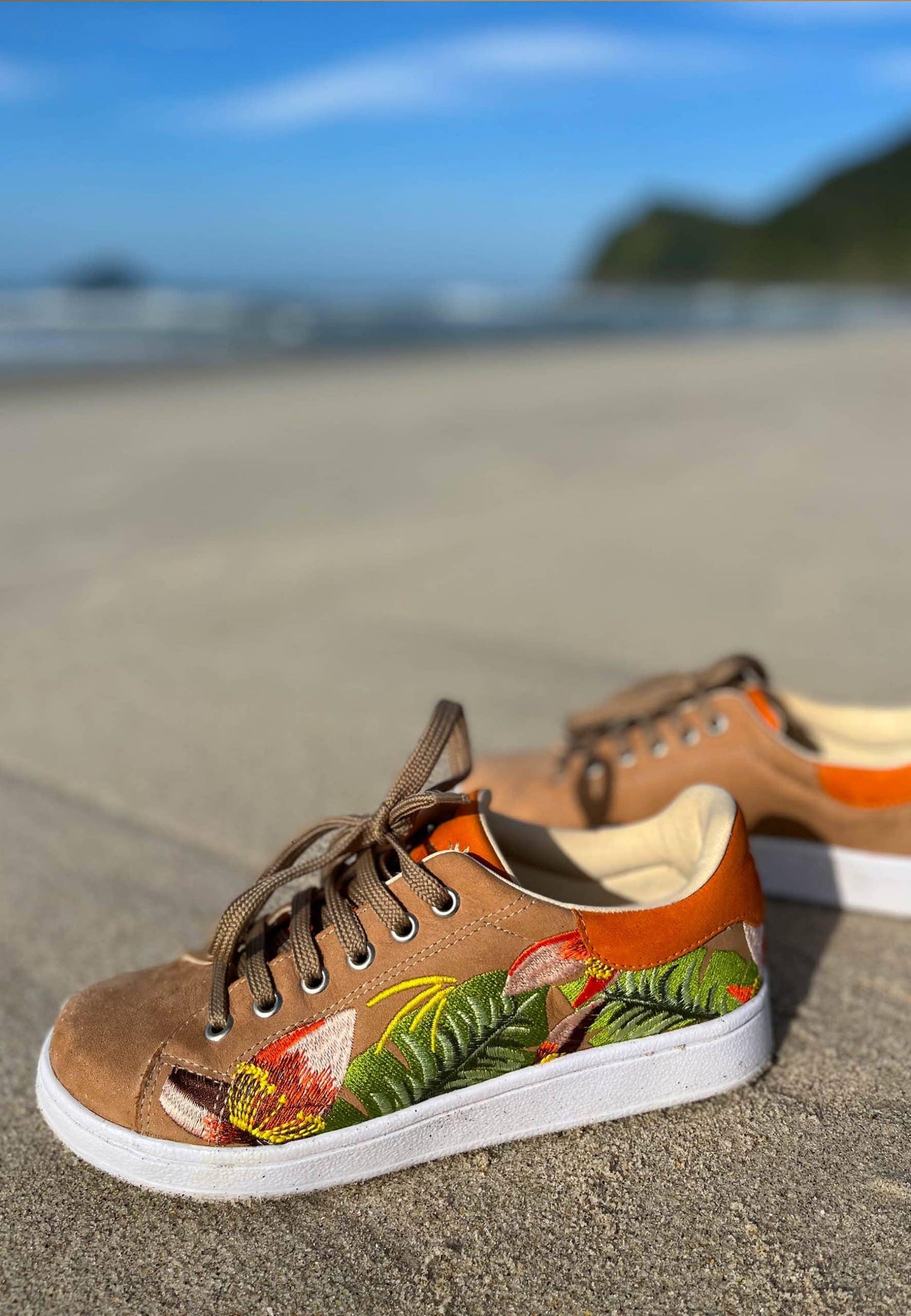 Pair of brown sneakers with floral design on a sandy beach