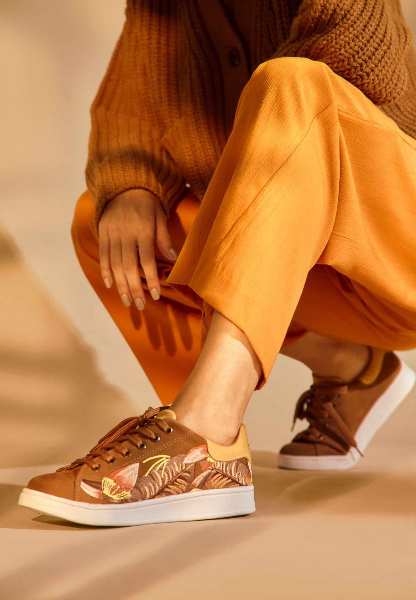 Person wearing brown patterned sneakers with orange pants and sweater on a beige background