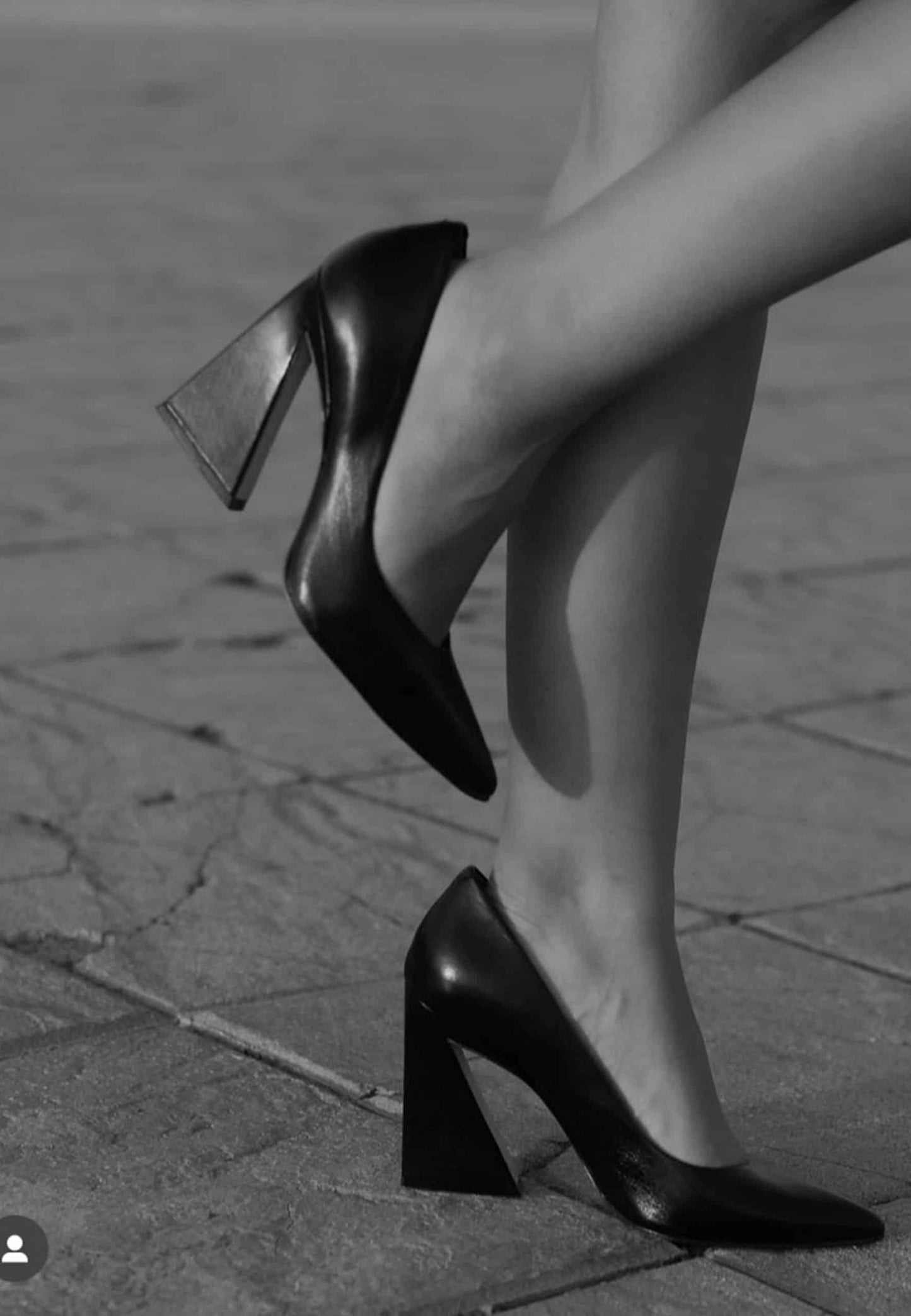 Black high-heeled shoes on a textured pavement