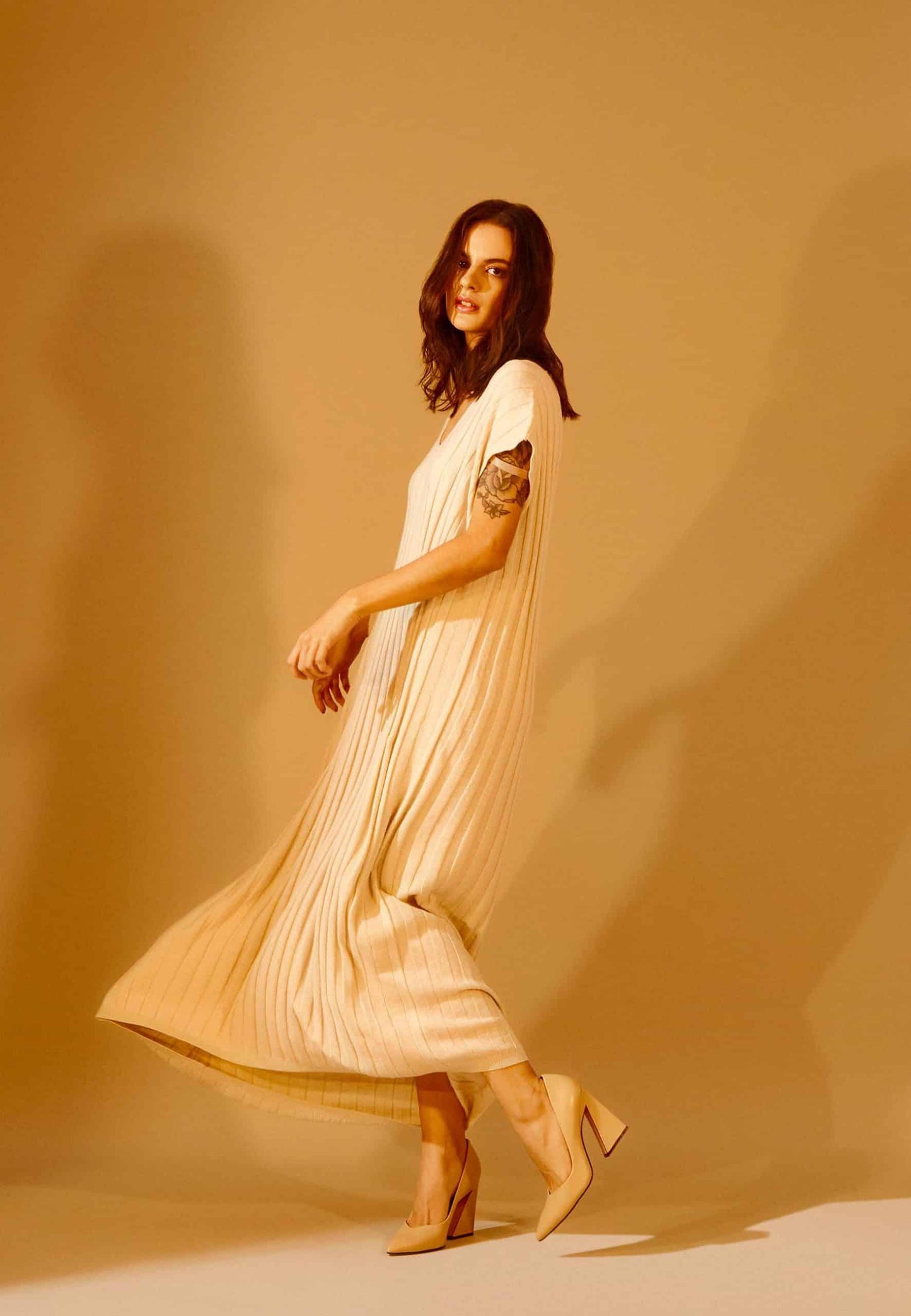 Woman in a flowing beige dress against a warm brown background
