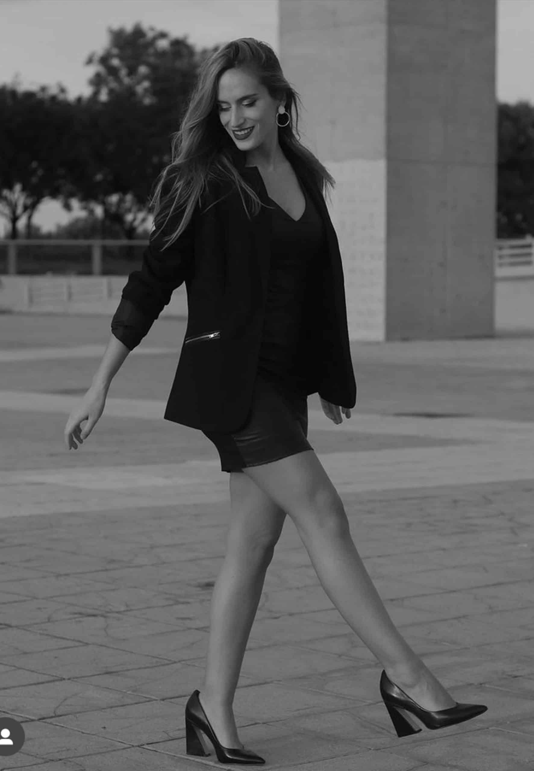 Woman in black outfit walking outdoors on a paved area with trees in the background