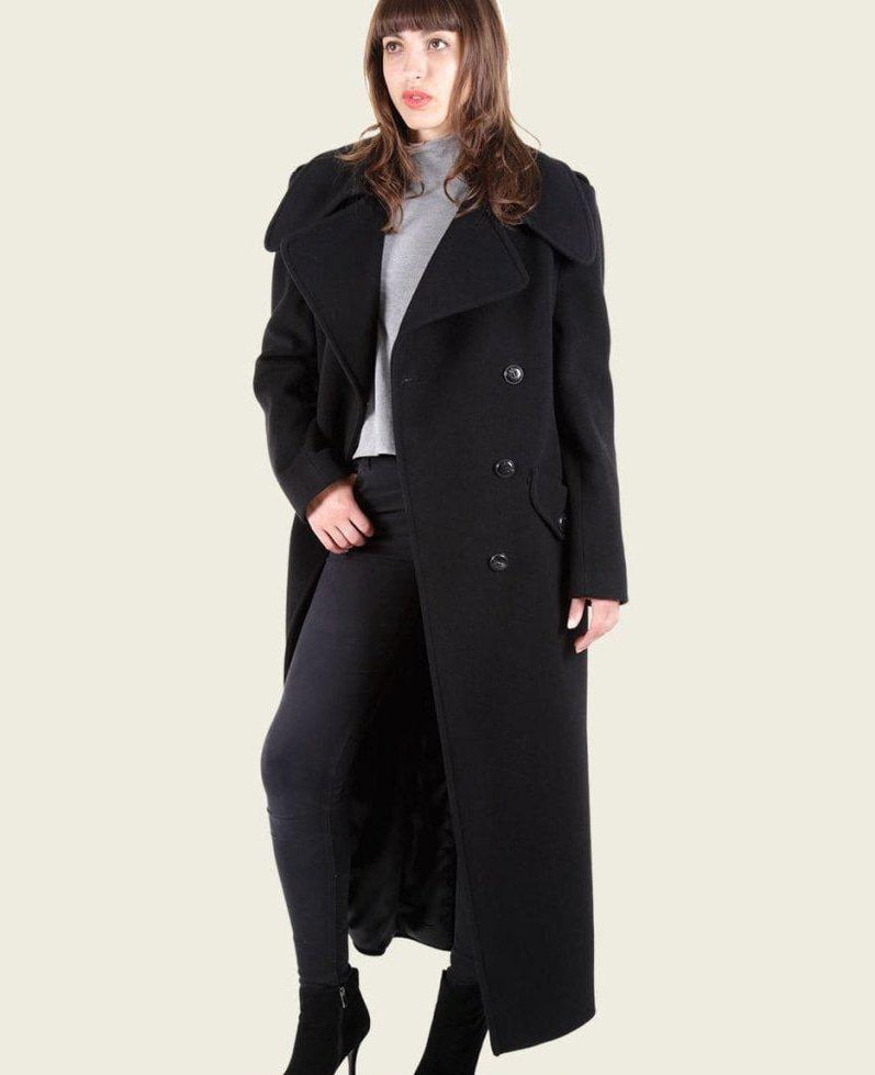 Woman wearing a long black coat on a plain background