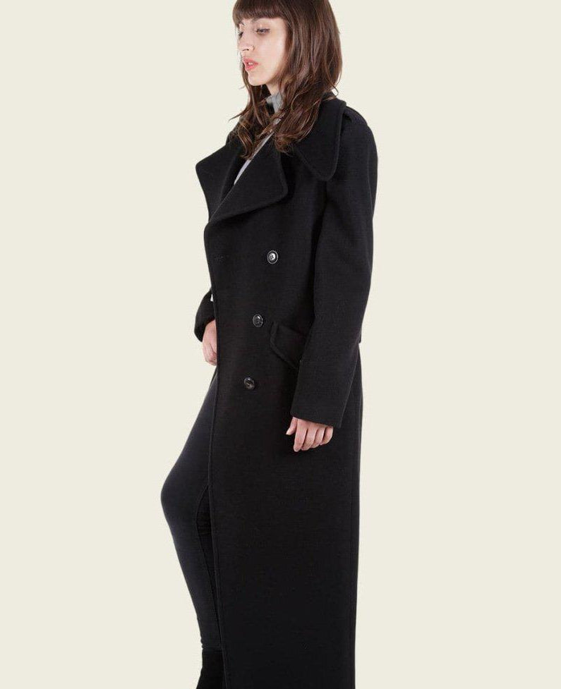 Woman wearing a long black coat on a plain background