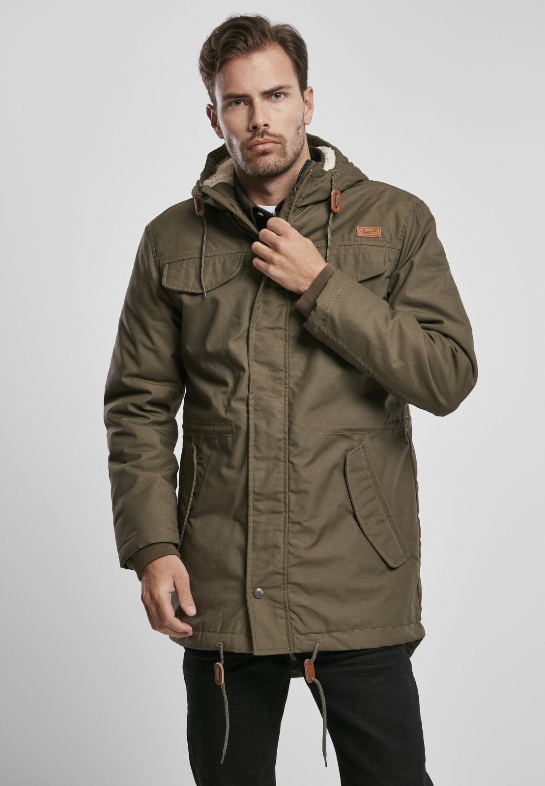 Man wearing a green parka jacket on a light gray background