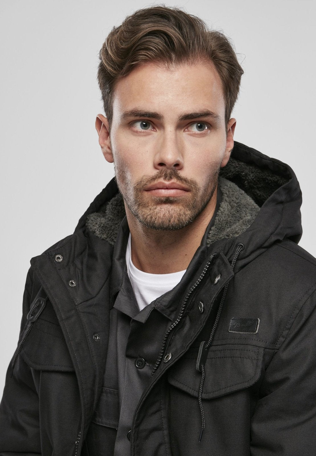 Man wearing a black coat with fur lining on a gray background