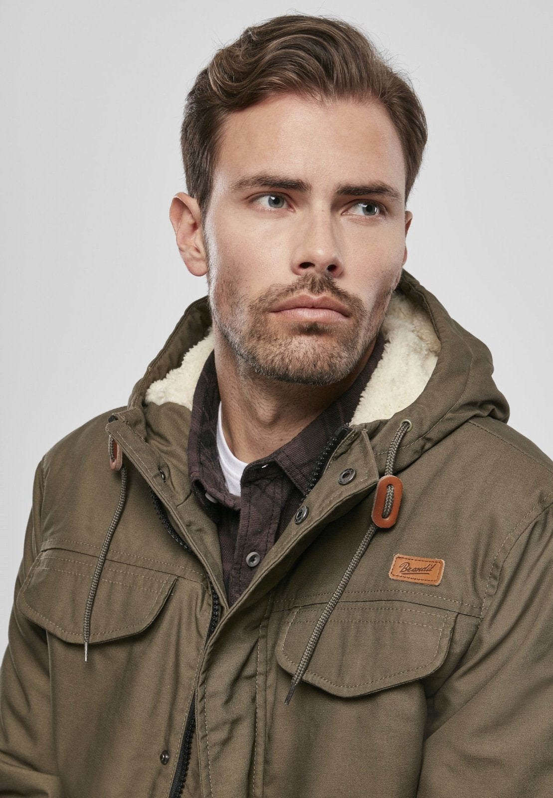 Man wearing a brown jacket with a hood on a plain background