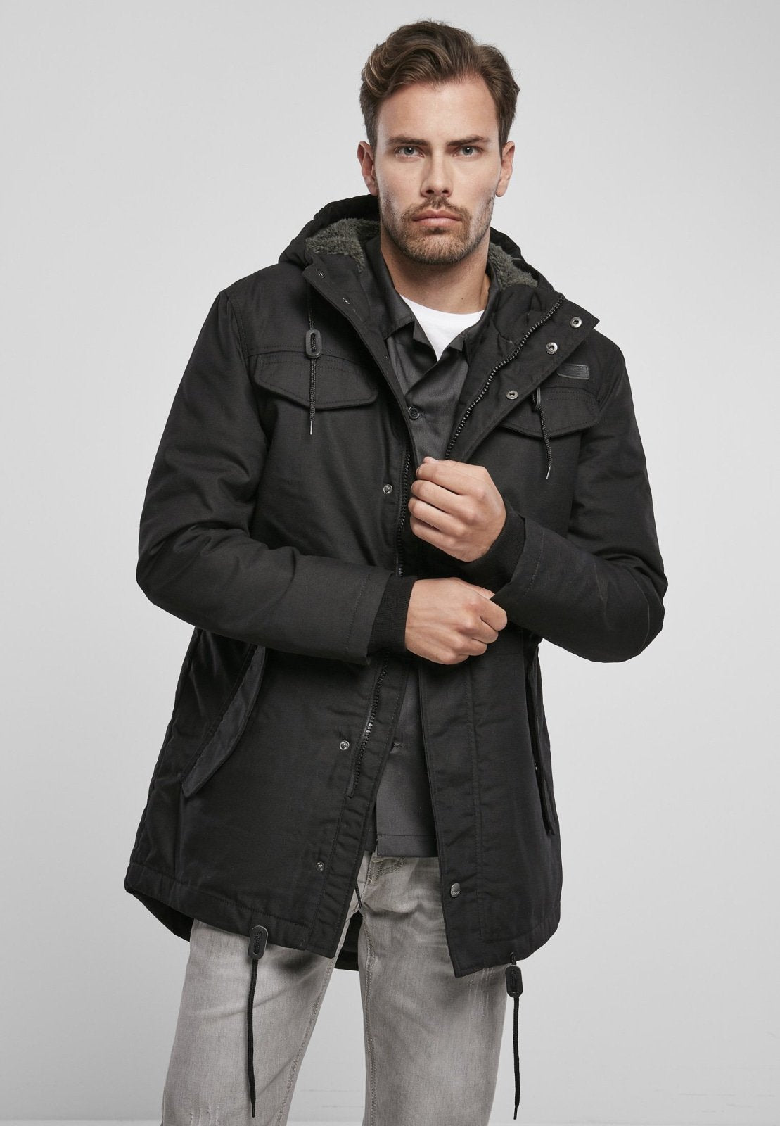Man wearing a black parka jacket on a light gray background