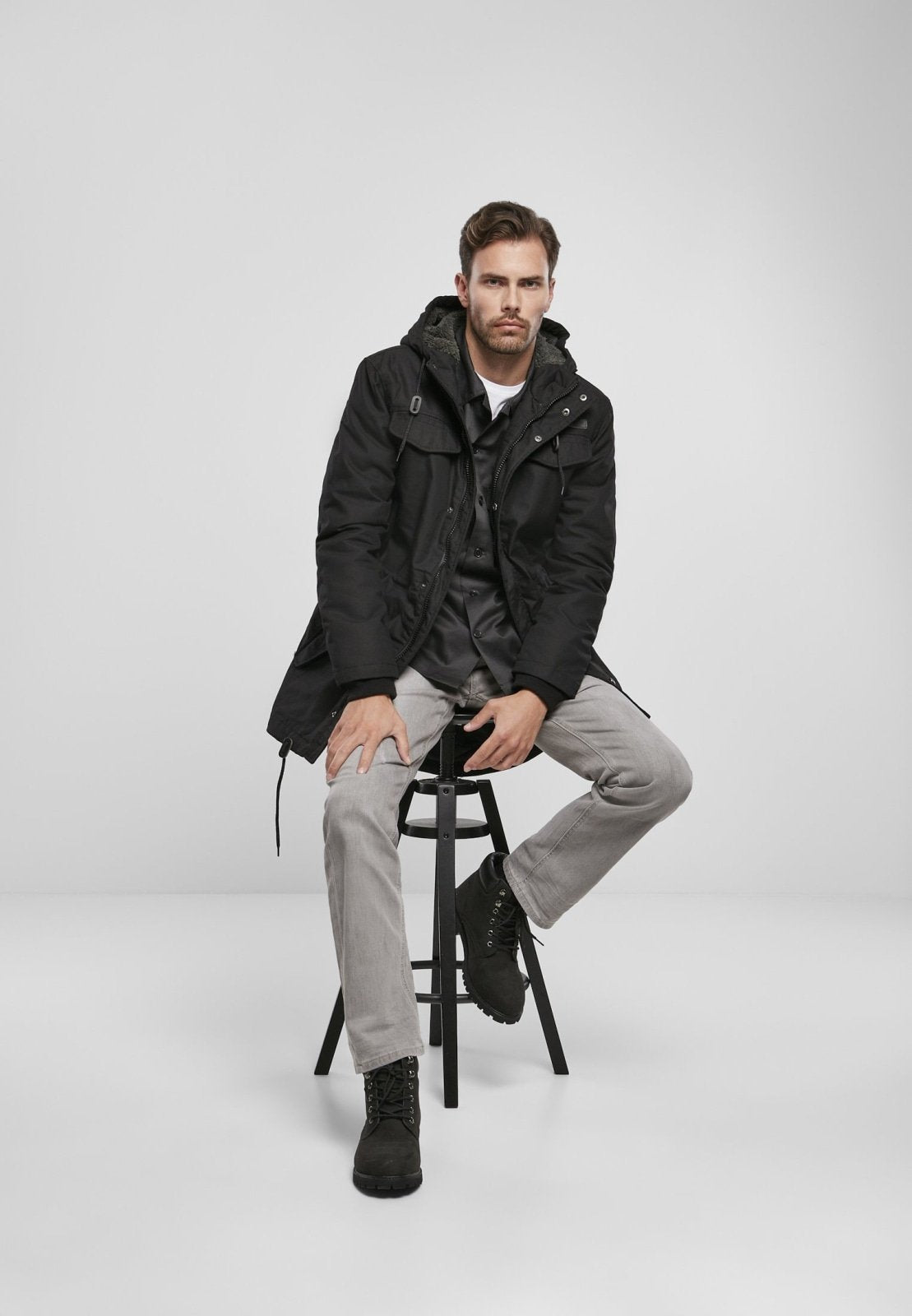 Man sitting on a stool wearing a black coat against a white background