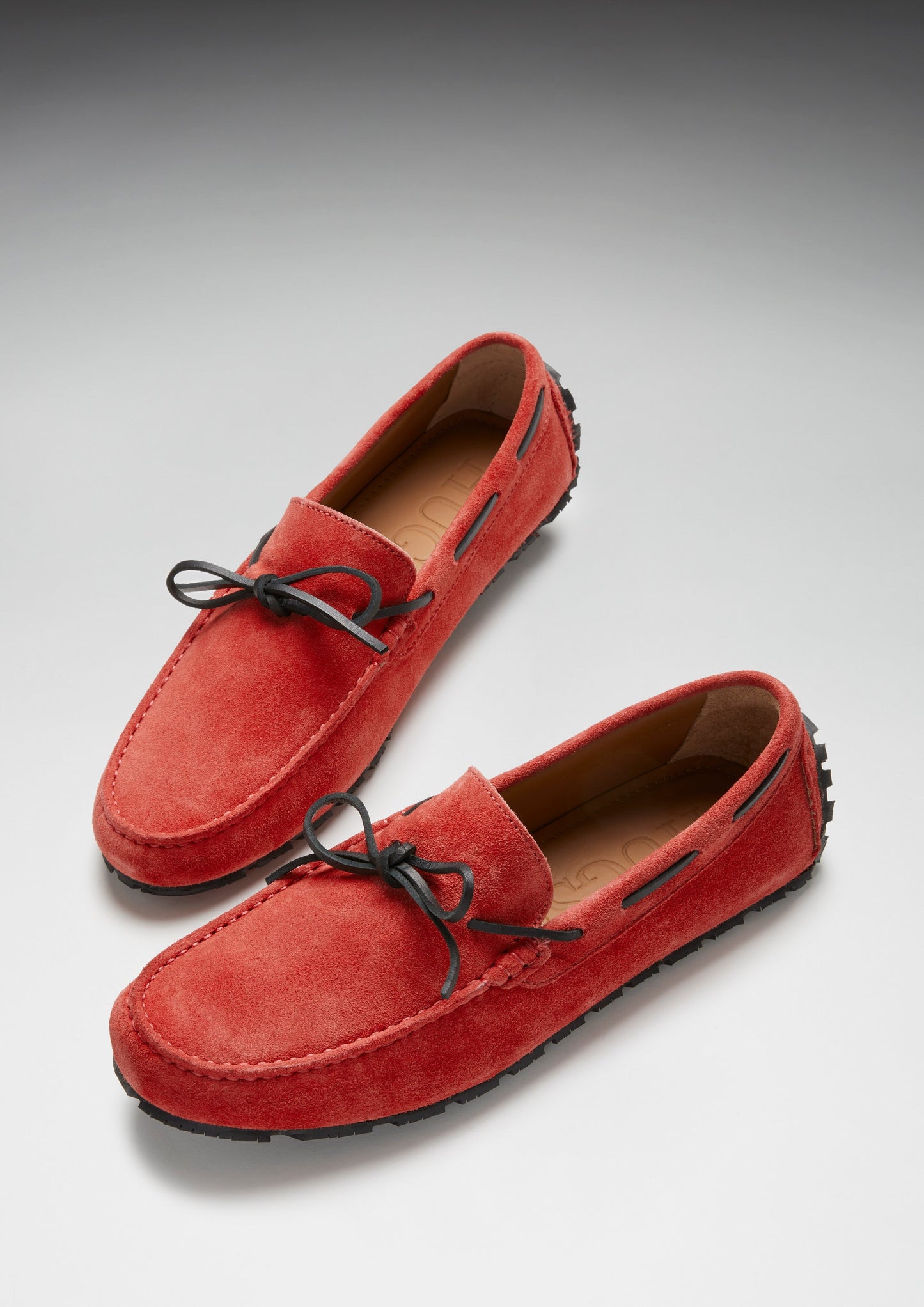 Red suede loafers with black laces on a light gray background
