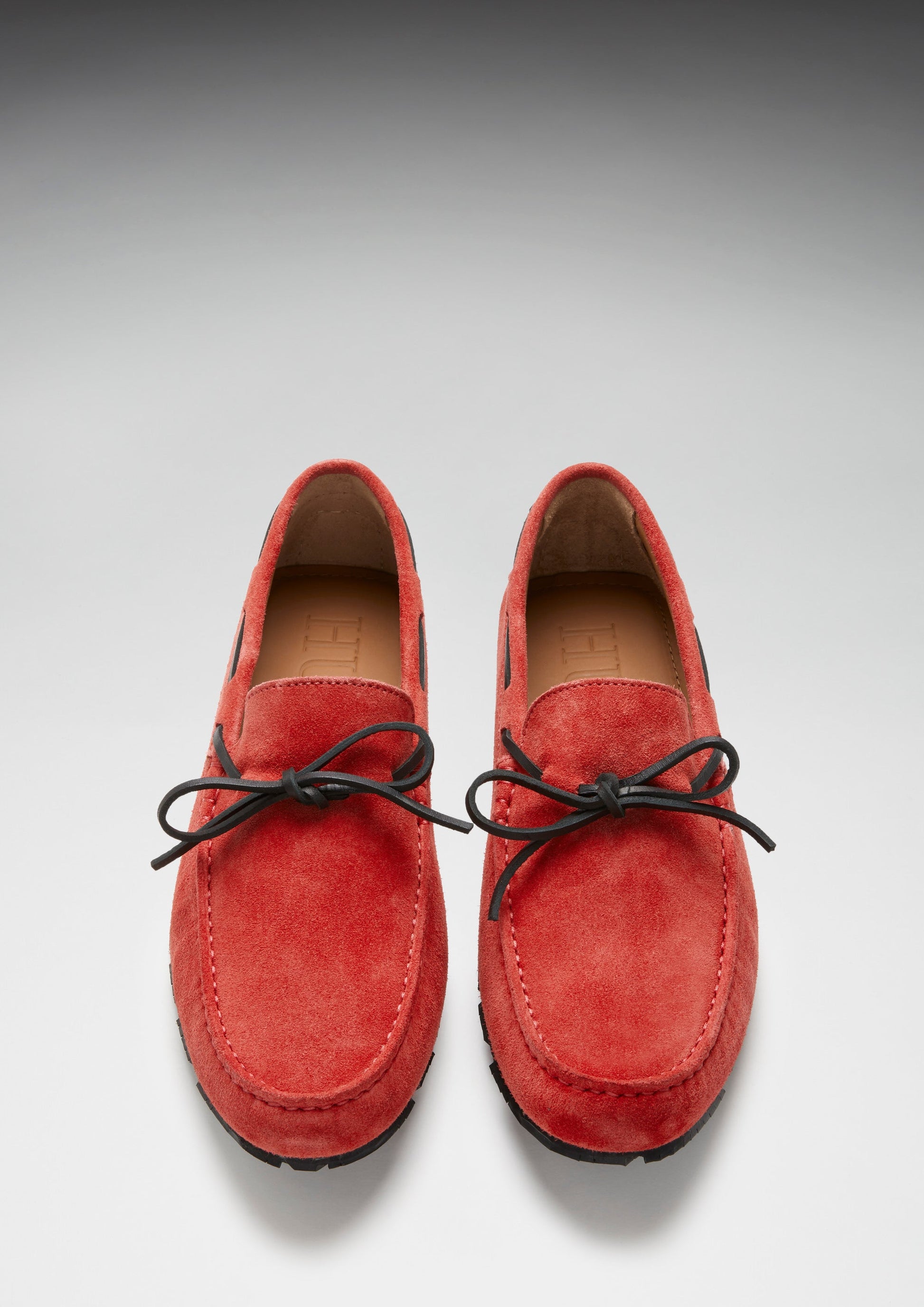 Pair of red suede loafers with black laces on a light gray background