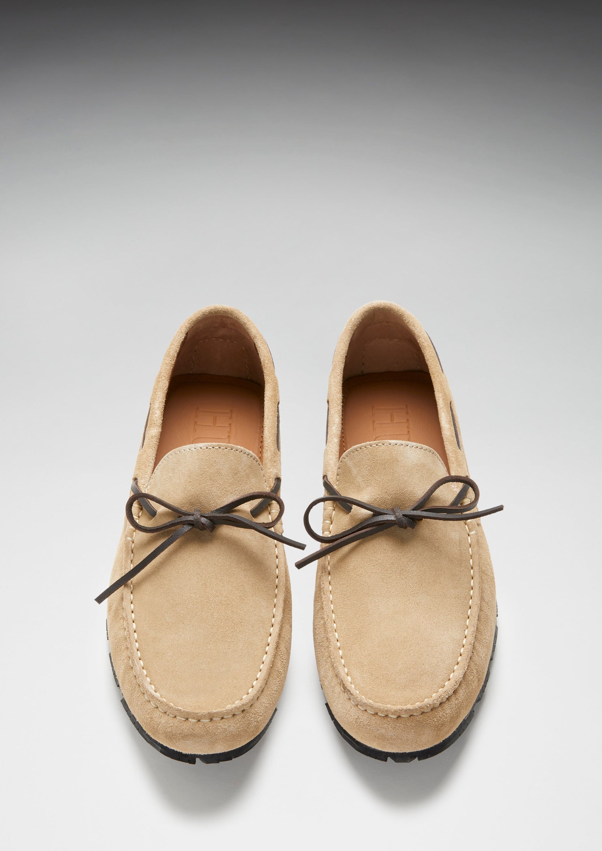 Pair of tan suede loafers with brown laces on a light gray background