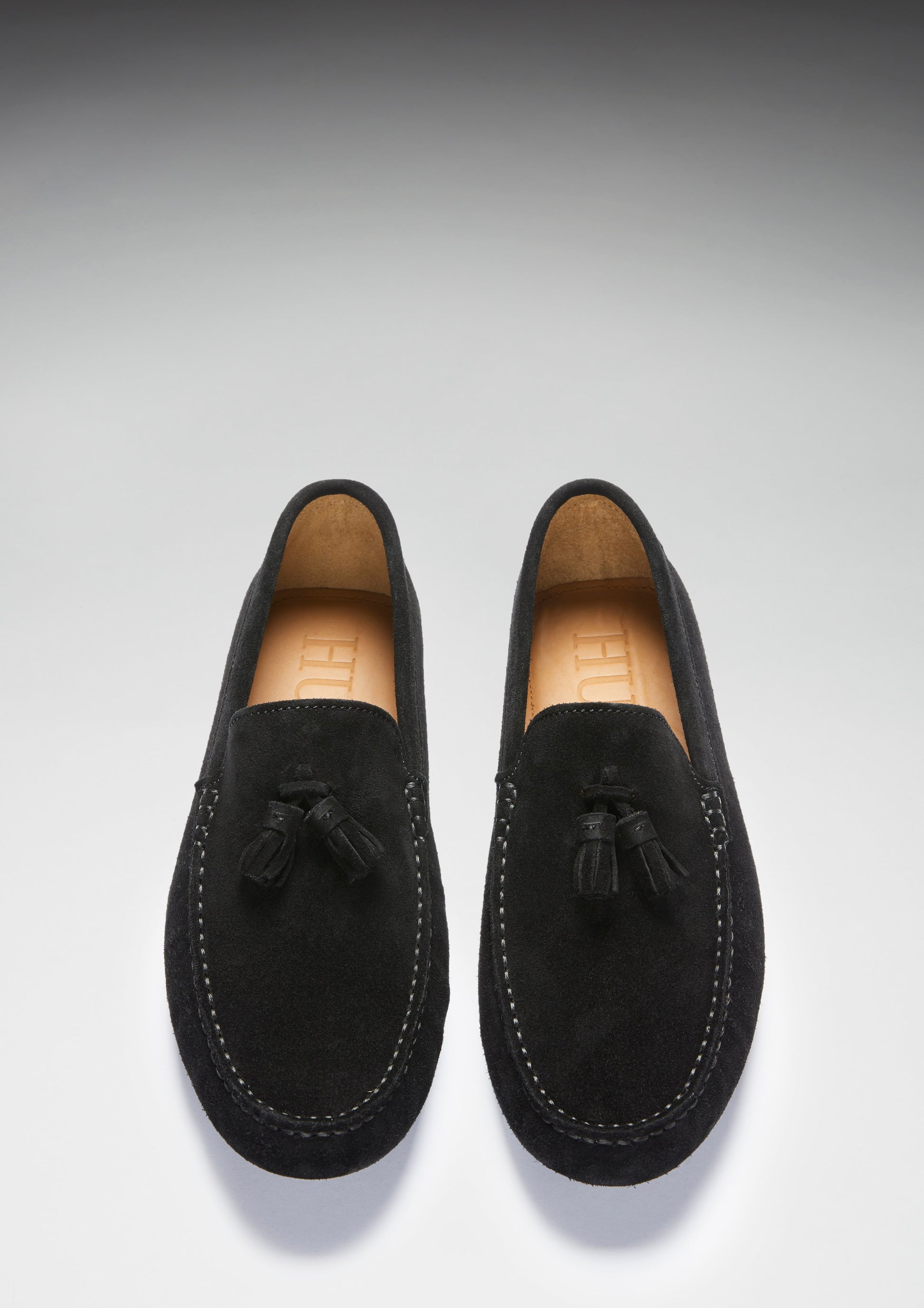 Pair of black suede loafers with tassels on a light gray background