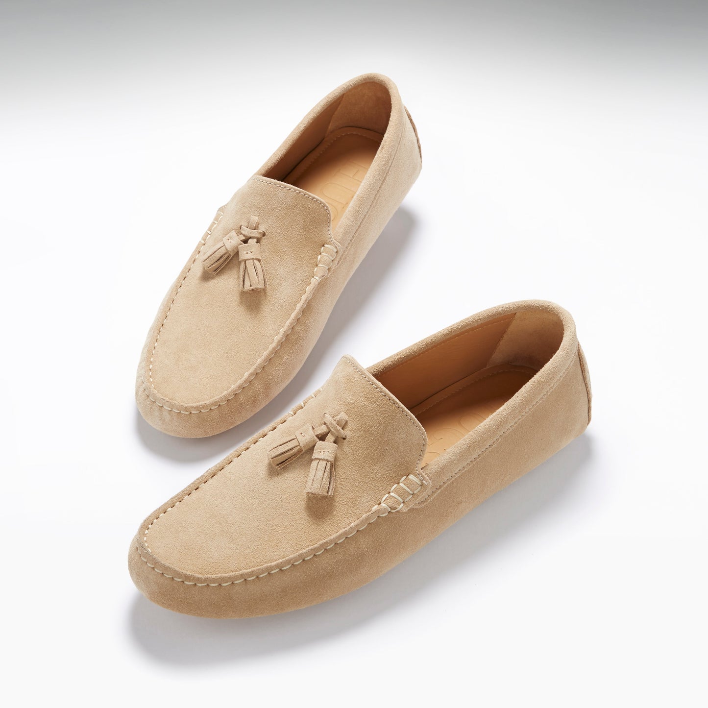 Pair of beige loafers with tassels on a white background