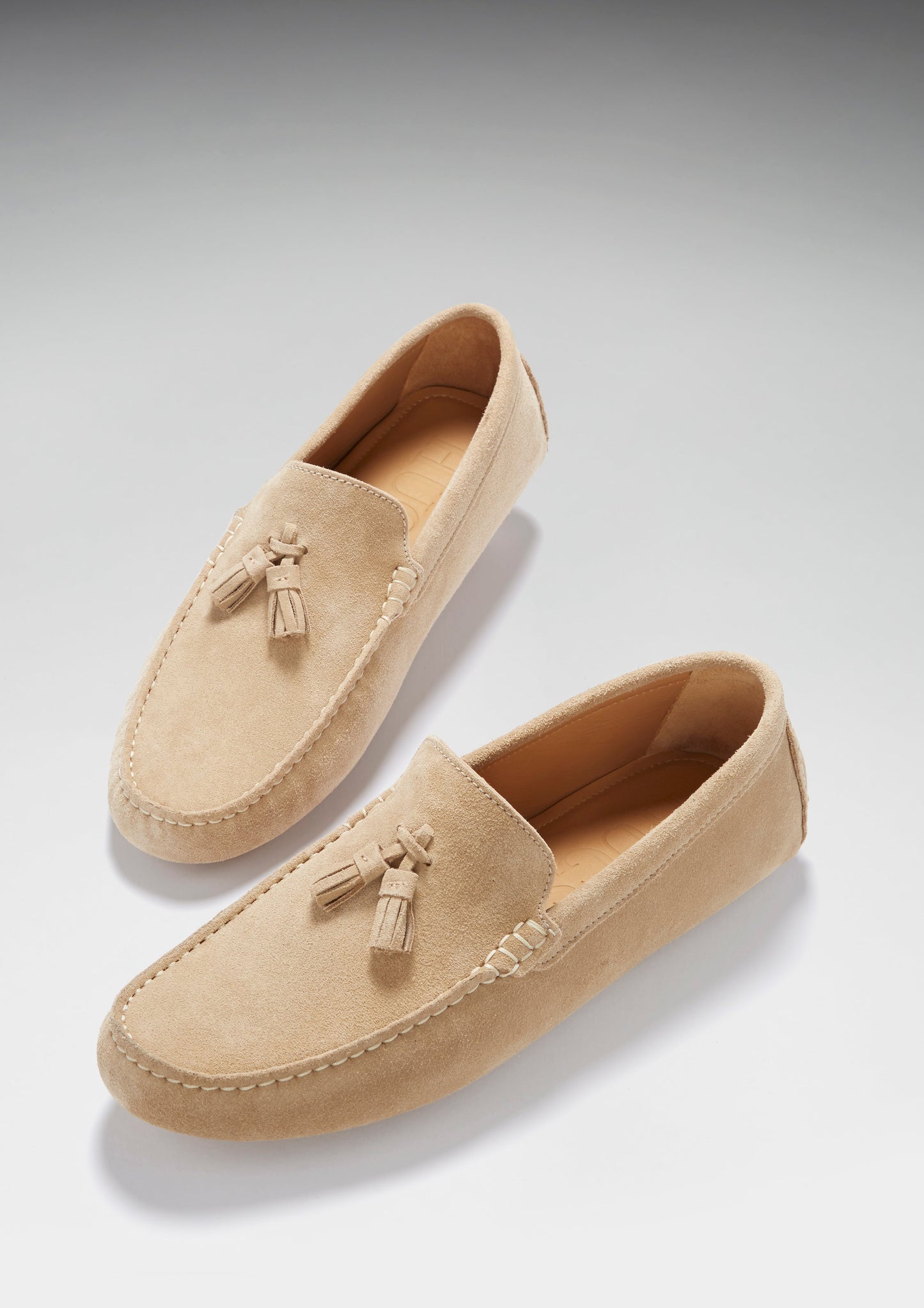 Pair of beige loafers with tassels on a light gray background