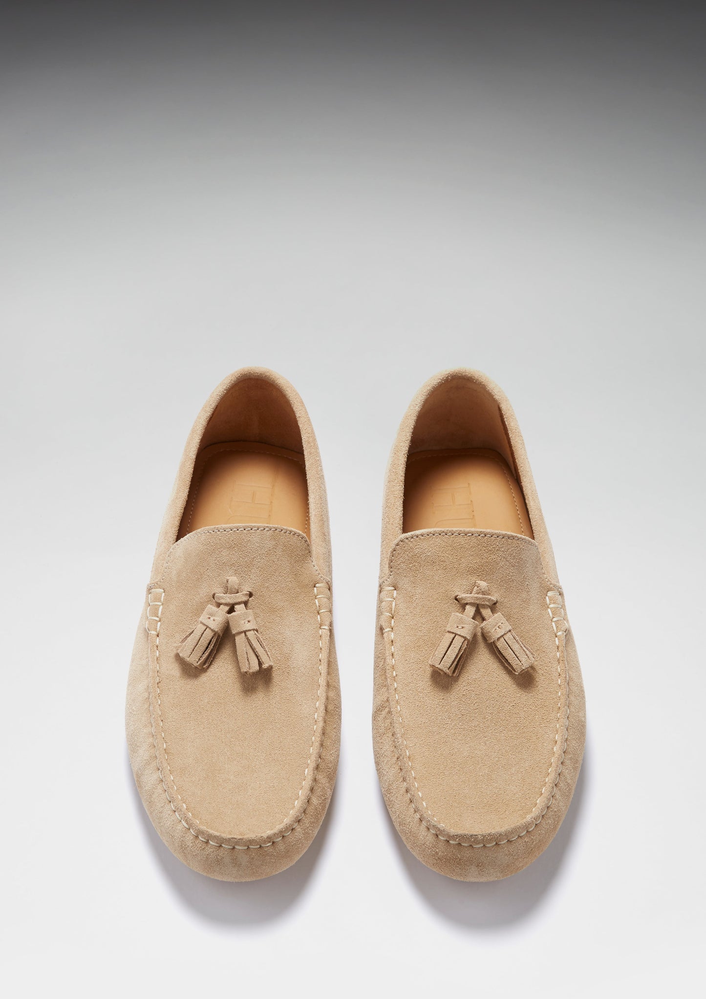 Pair of tan loafers with tassels on a light gray background
