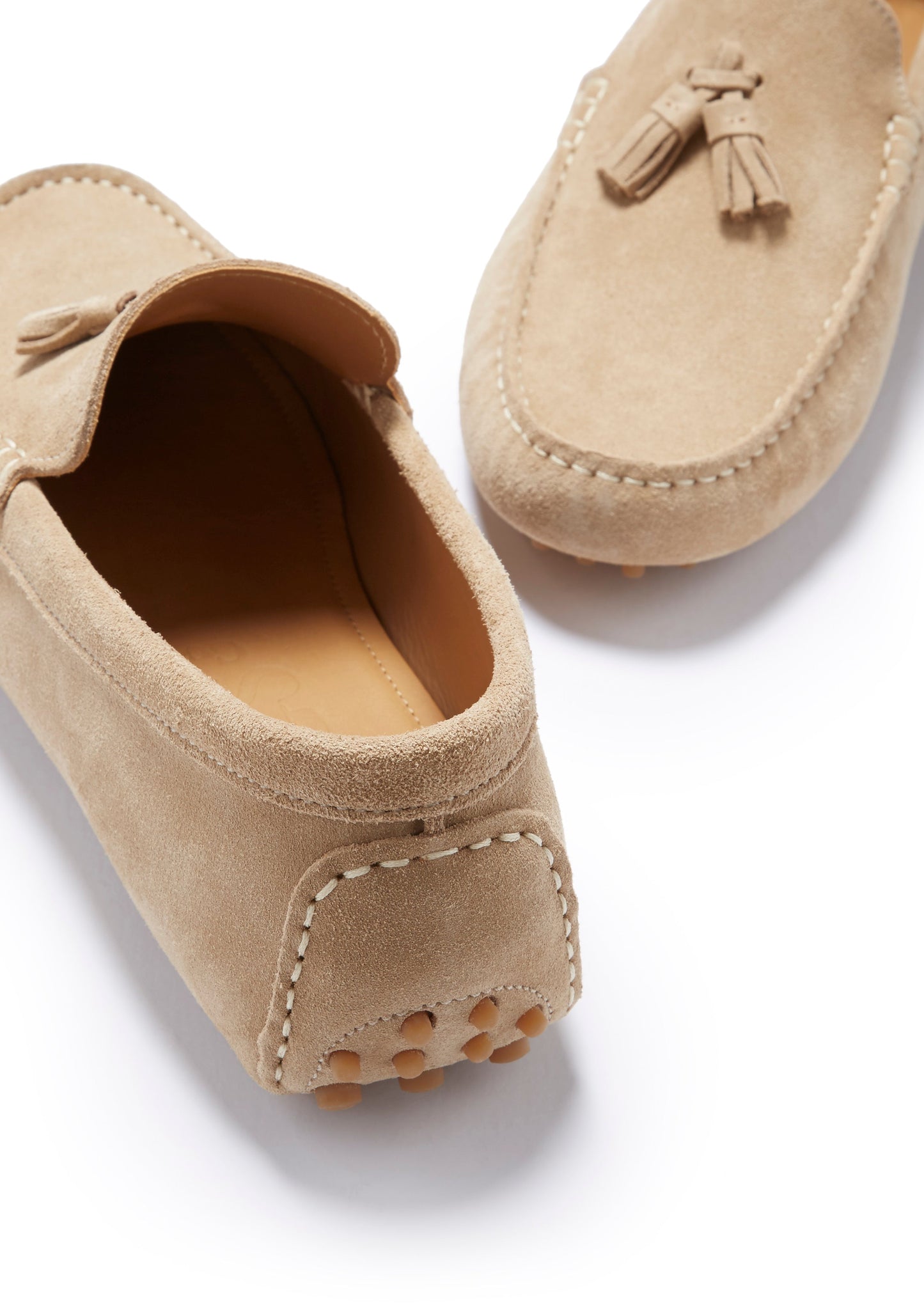Pair of beige suede loafers with tassels on a white background