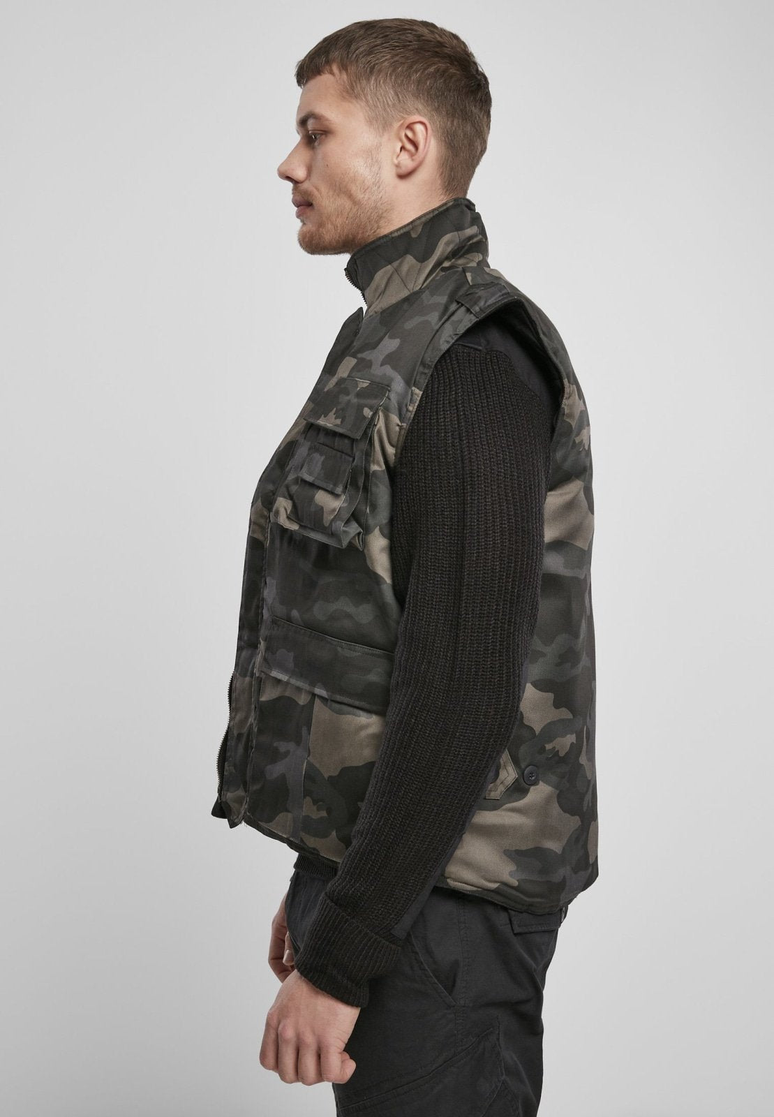 Man wearing a camouflage vest over a black sweater on a white background