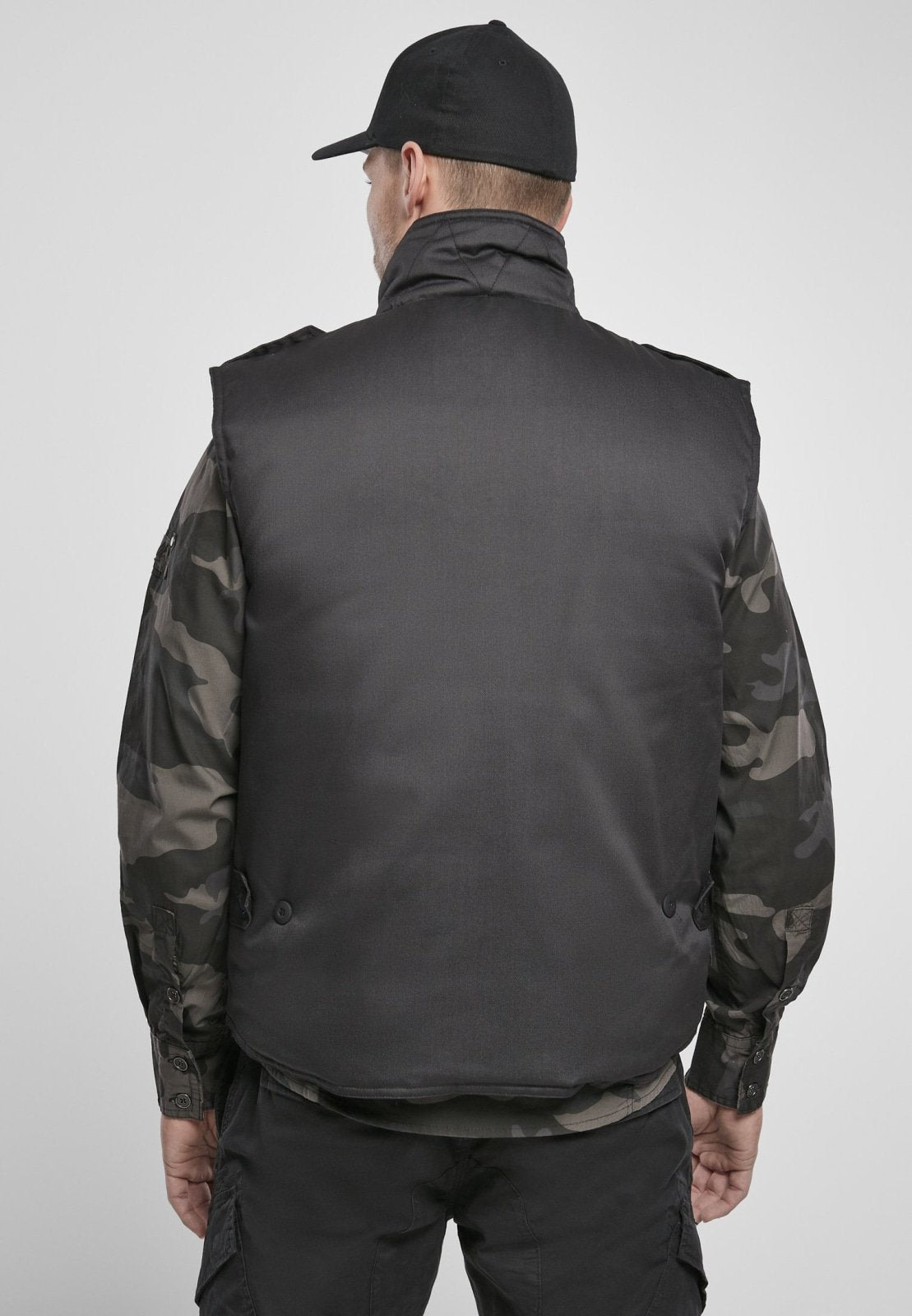 Person wearing a black vest over camouflage sleeves on a plain background