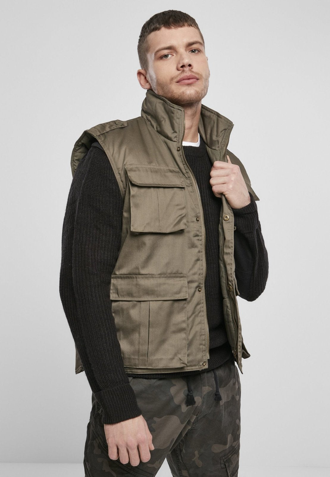 Man wearing a green vest over a black sweater on a white background