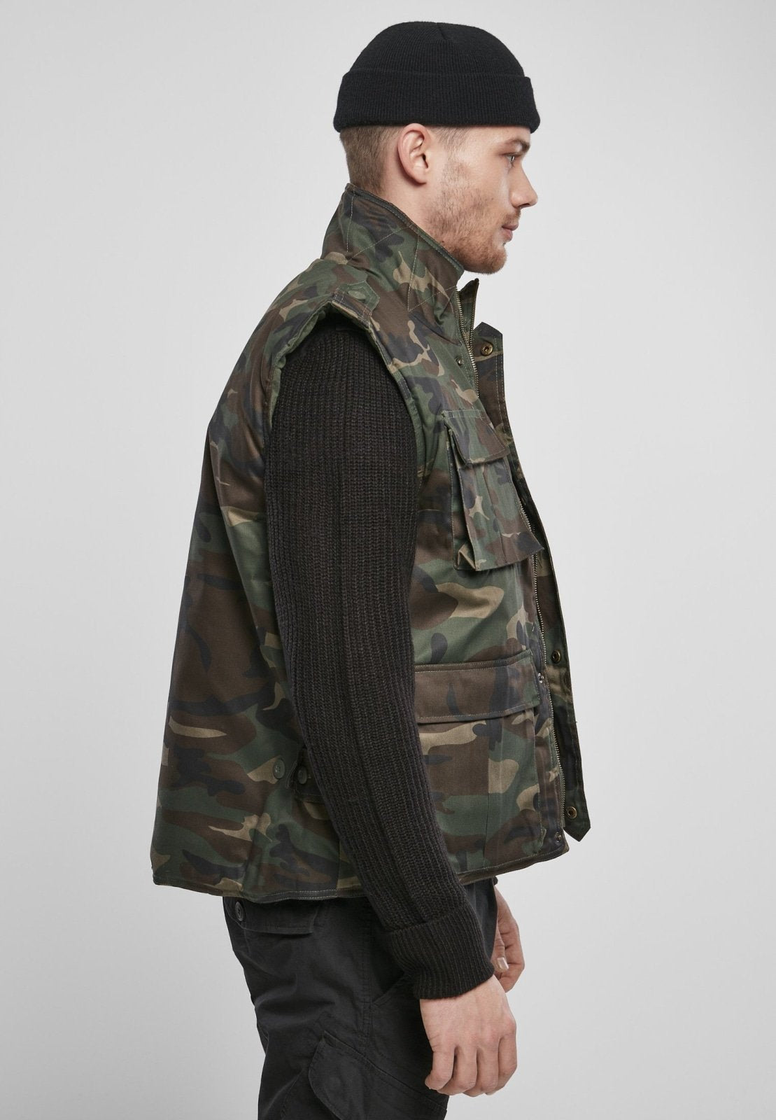 Person wearing a camouflage vest over a dark sweater on a plain background