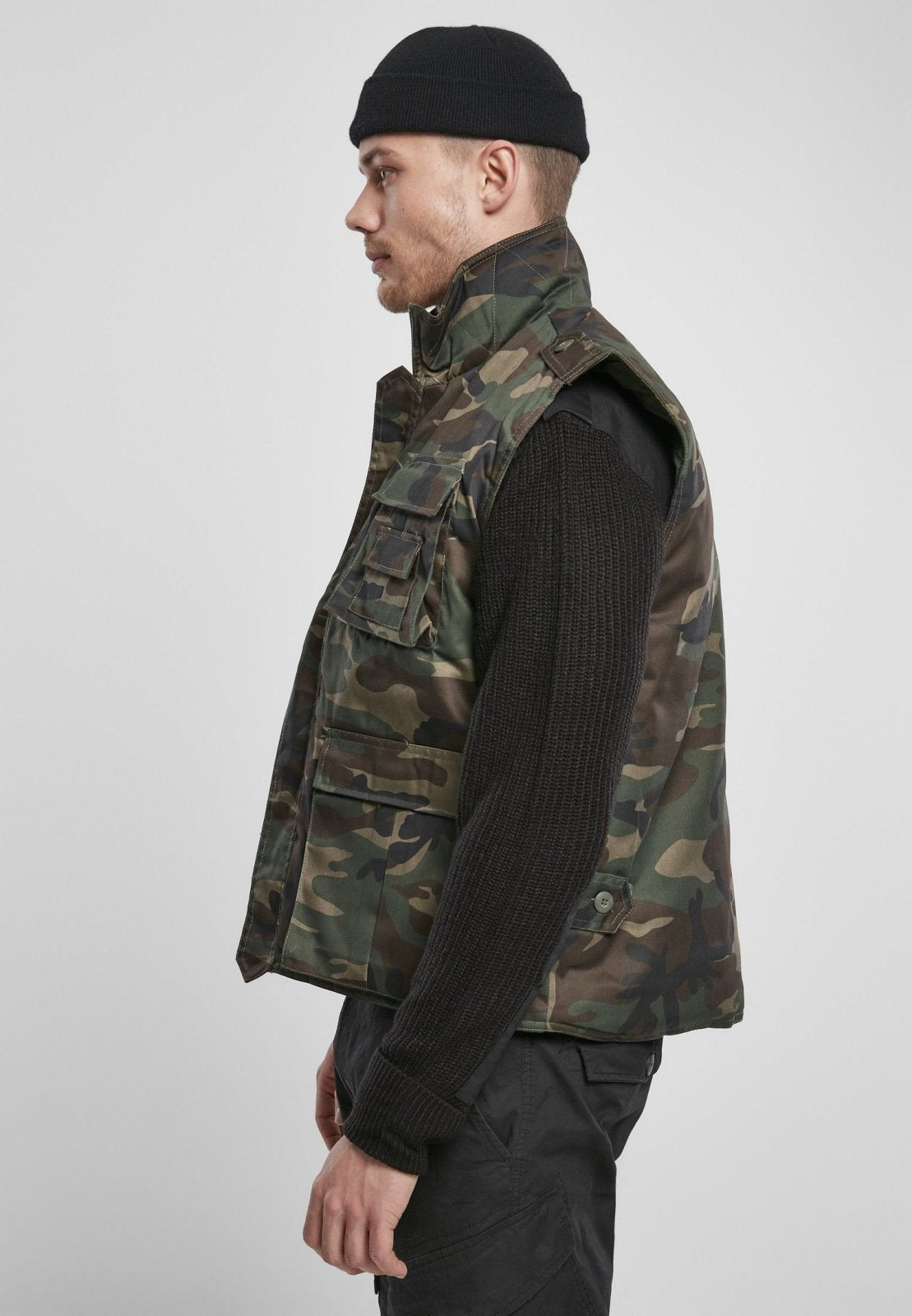 Man wearing a camouflage vest over a black shirt on a white background