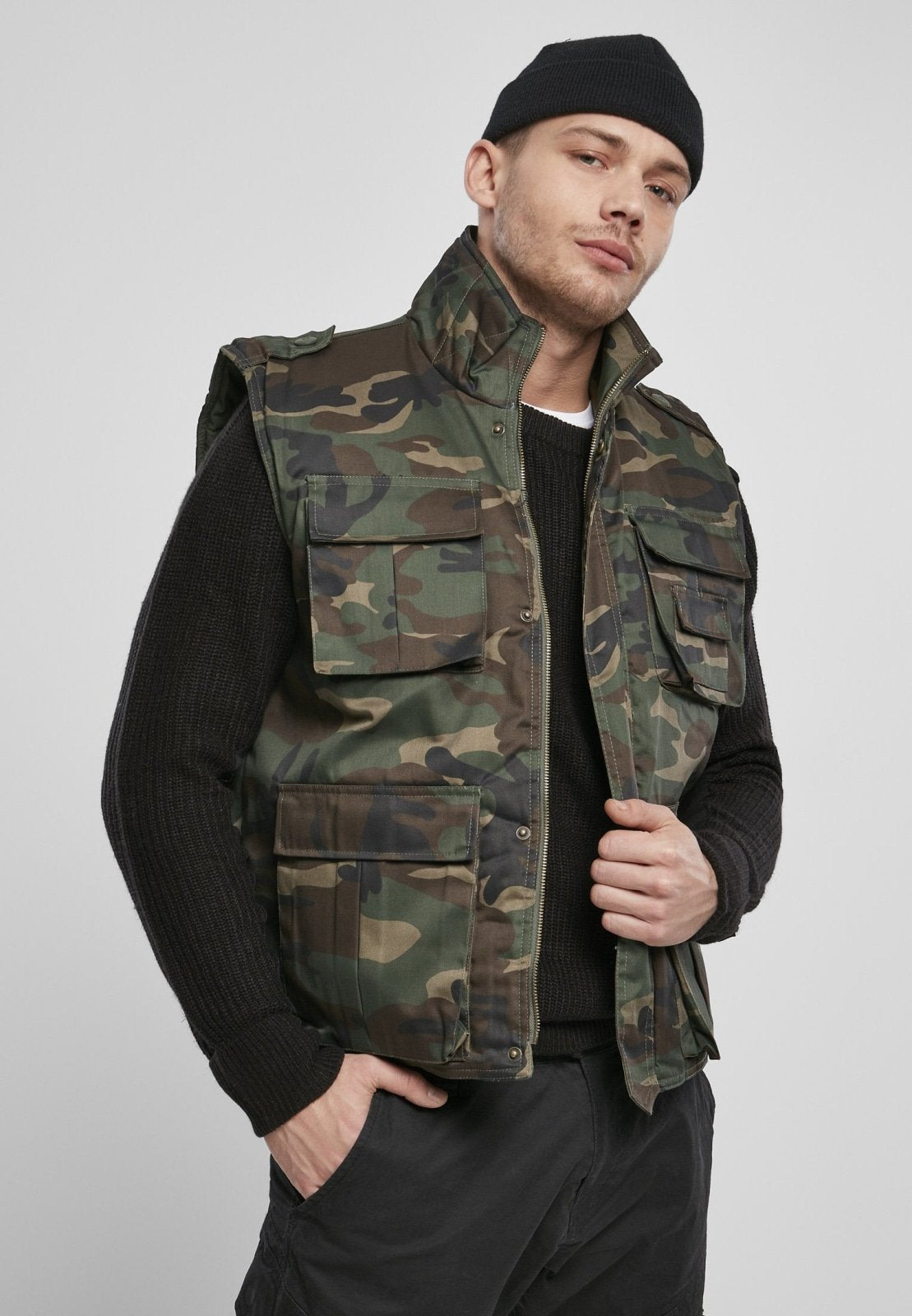 Man wearing a camouflage vest over a black shirt on a plain background